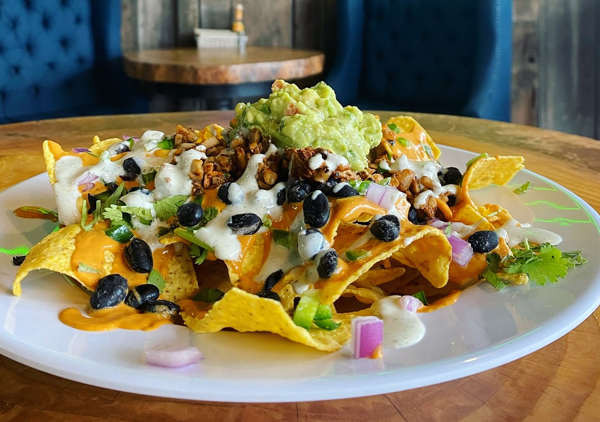Plate of nachos topped with lettuce, black beans, cheese, and sour cream, garnished with lemon slices and chopped onions.
