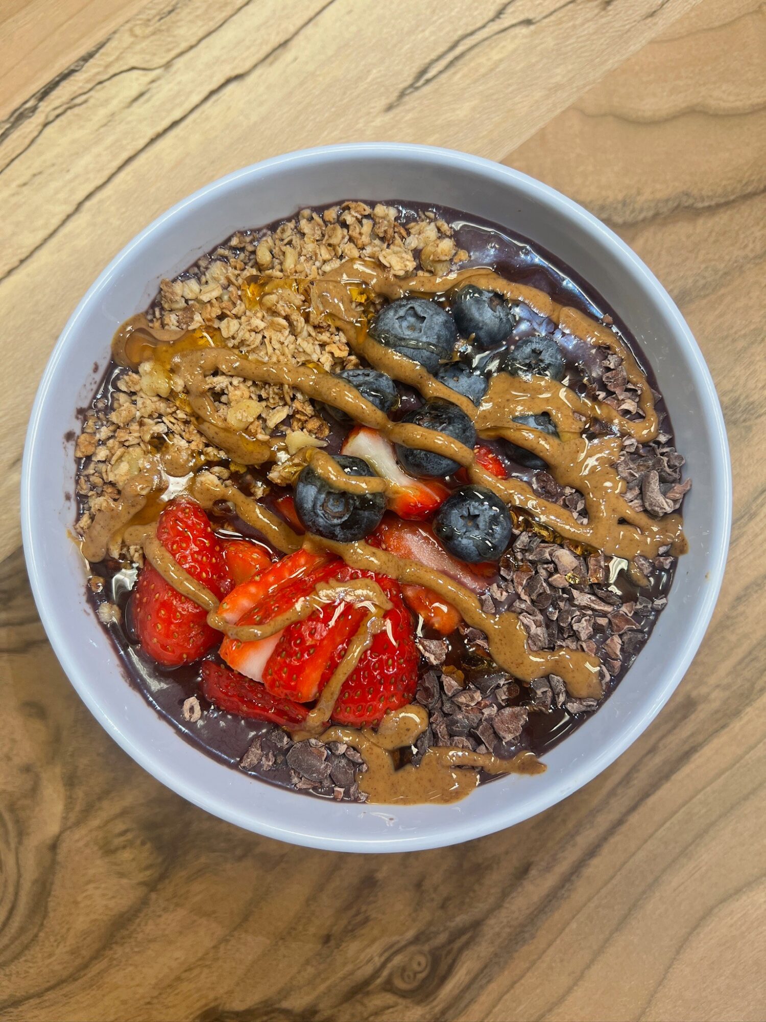 Bowl of yogurt topped with strawberries, blueberries, granola, and drizzled with caramel sauce on a wooden surface.