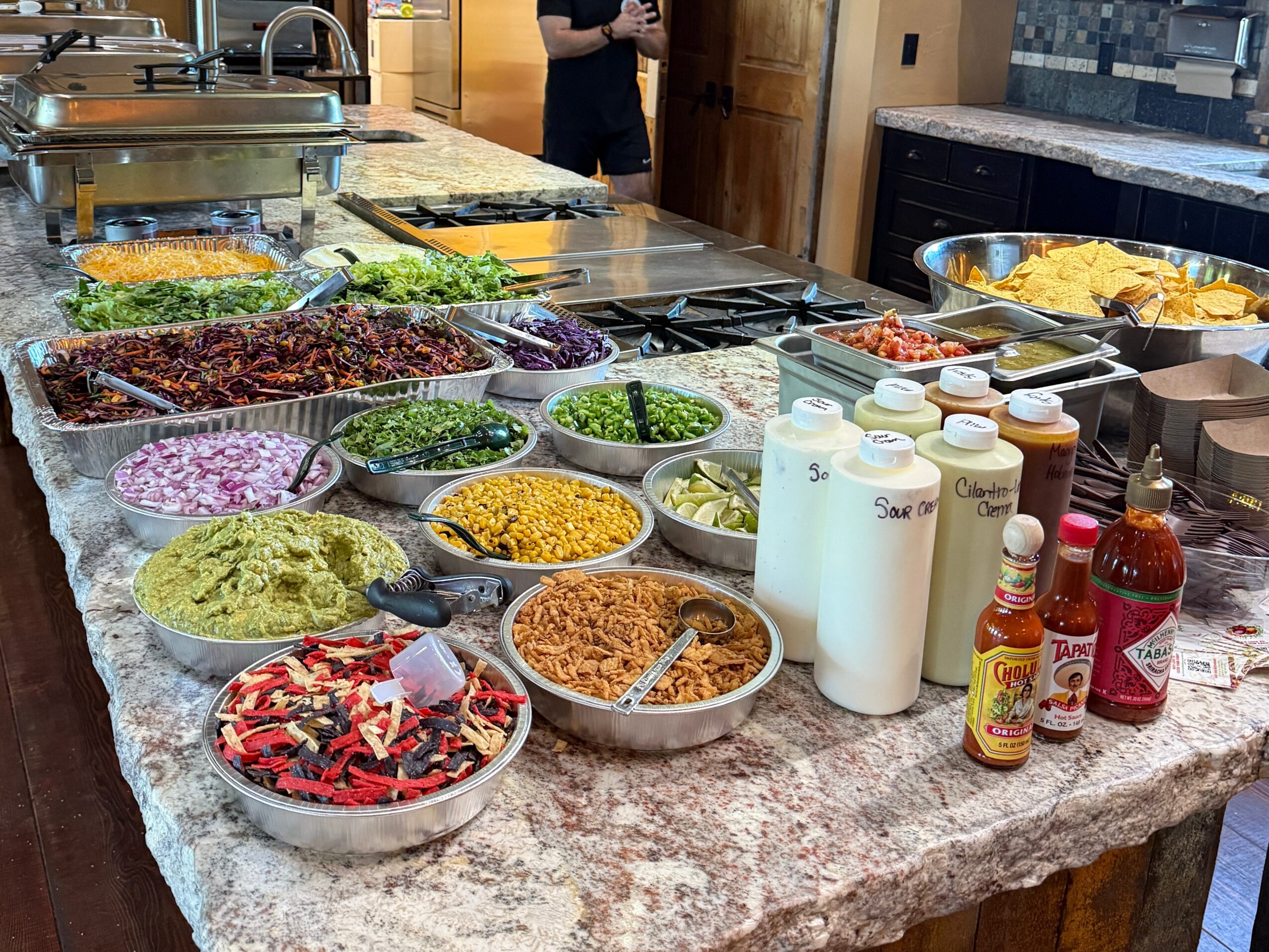 Counter with various bowls of colorful salads, toppings, and condiments in a kitchen setting.