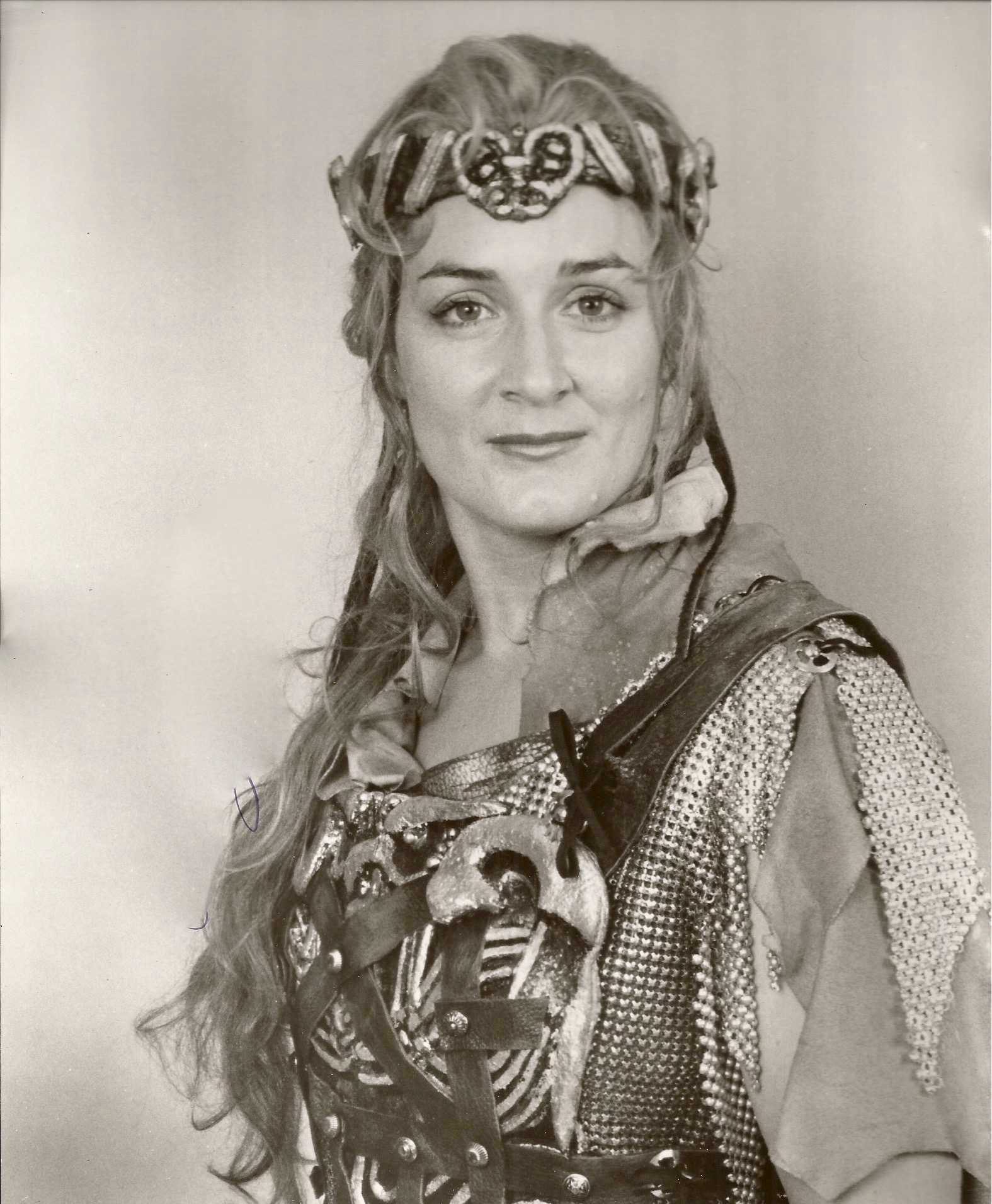 Woman with long wavy hair wearing a decorative headpiece and medieval-style costume, smiling at the camera.