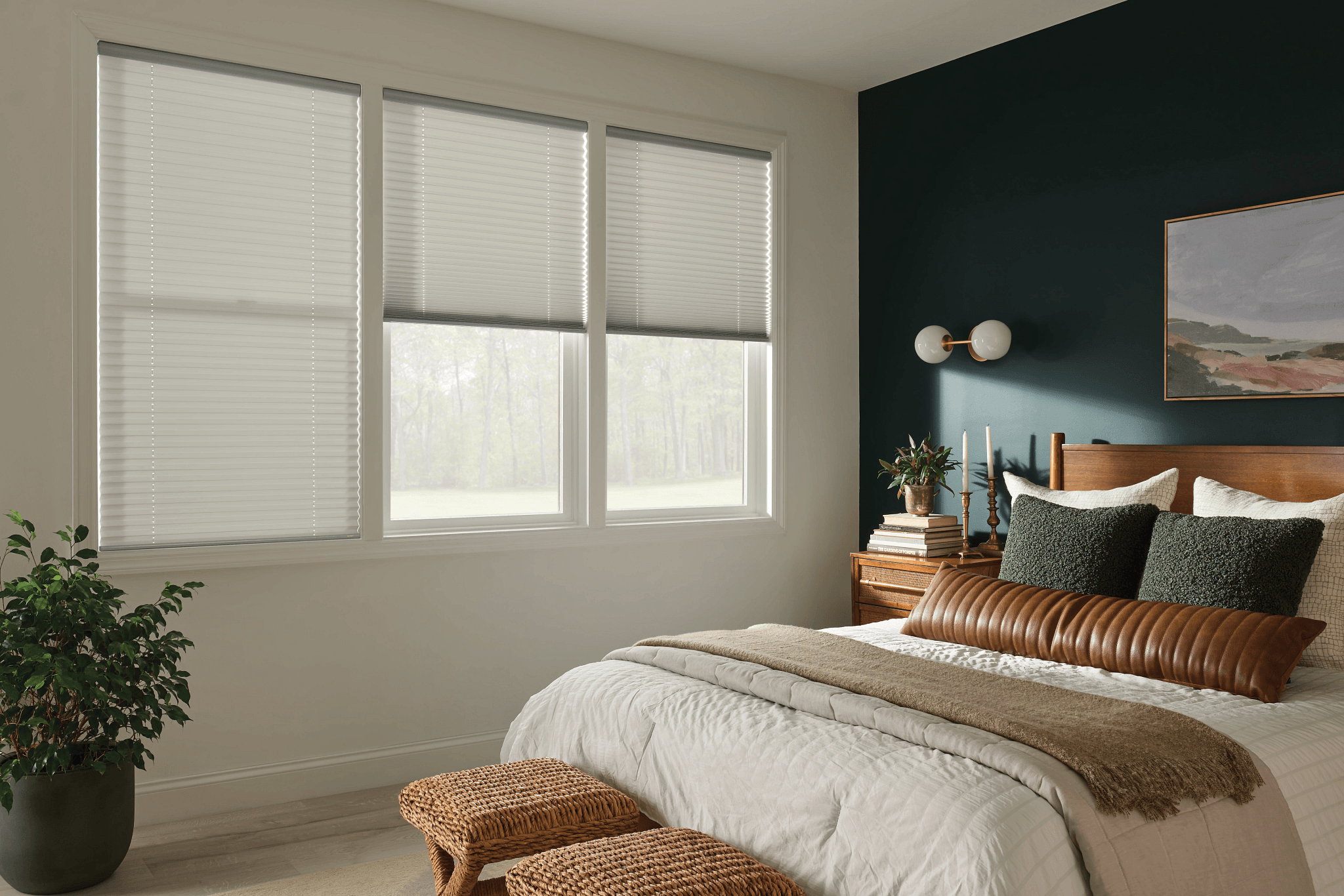 Bedroom with large window, bed with pillows, nightstand, and wall art, natural light coming in.