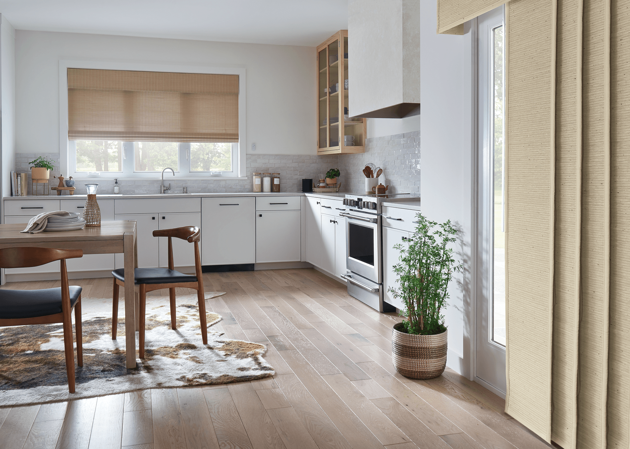 Bright kitchen with white cabinets, wooden floor, window with beige blinds, and a potted plant near a glass door.