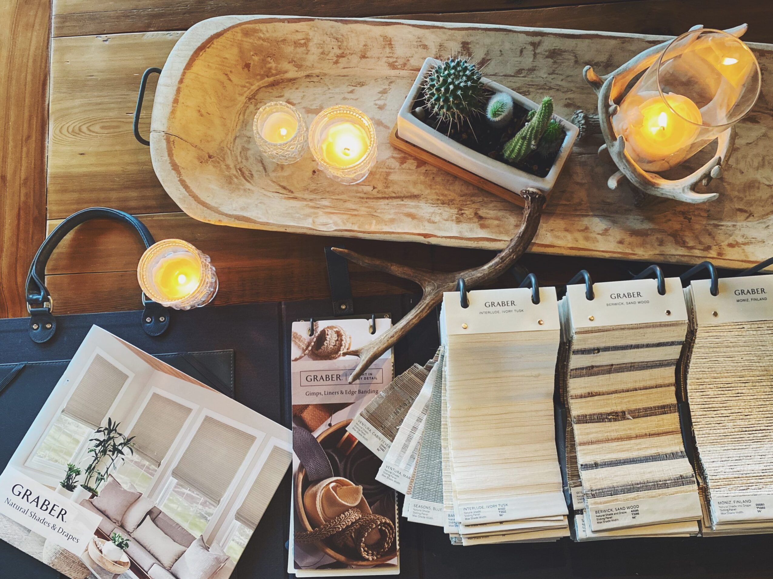 Table with candles, a phone, plant samples, a magazine, and color swatches, viewed from above.
