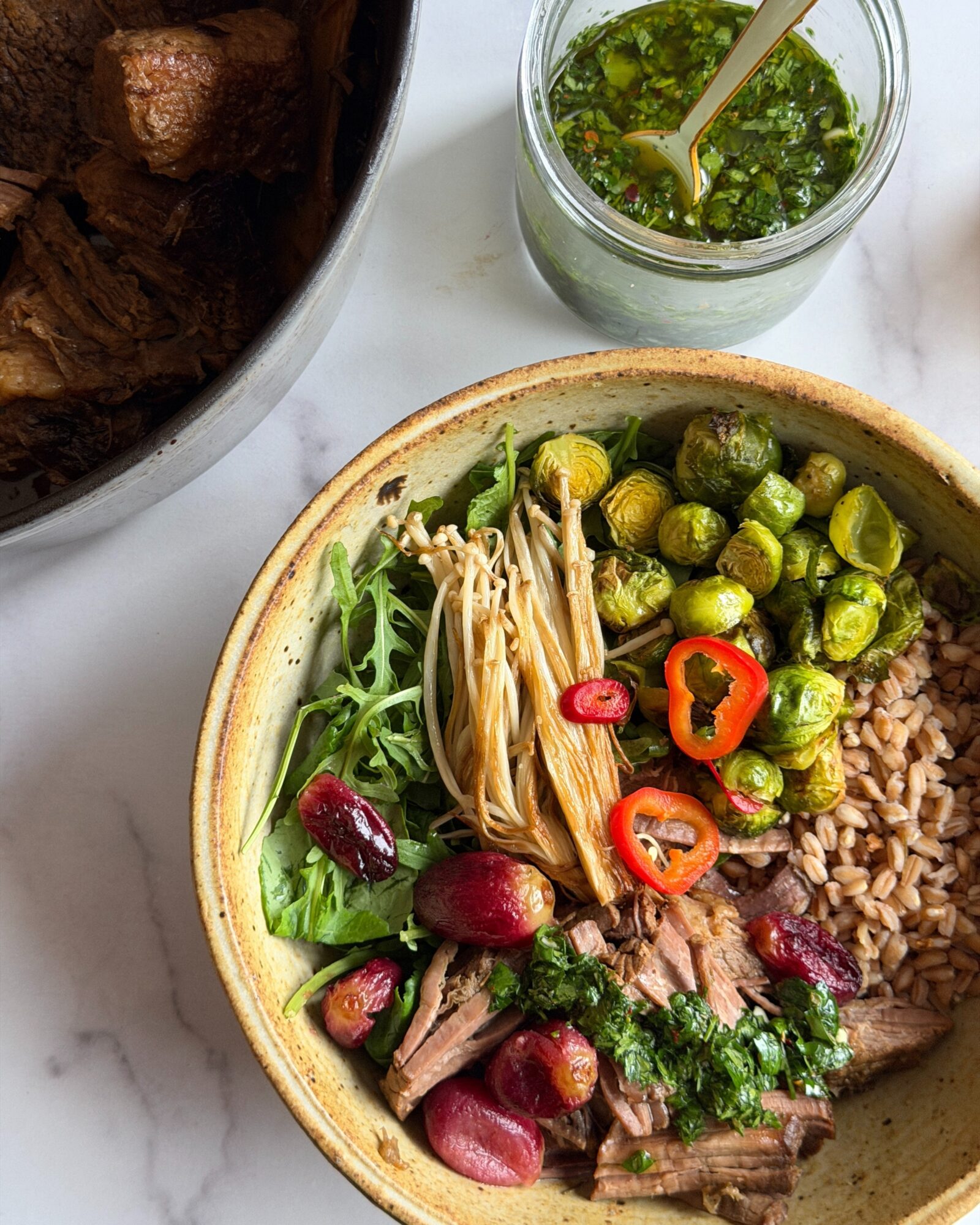 Bowl with rice, vegetables, and shredded meat, with a small jar of green sauce and a glass of green condiment nearby.