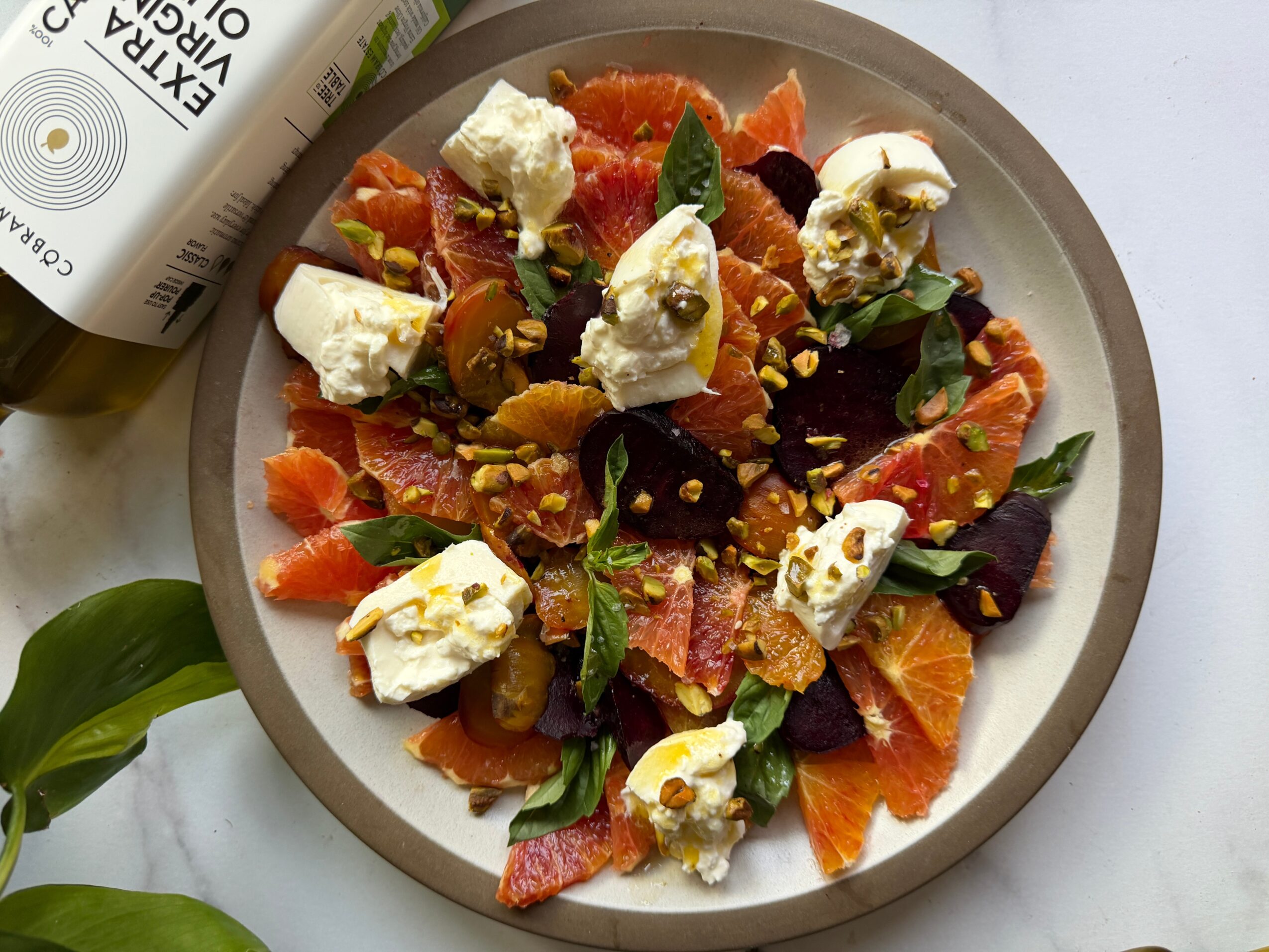 Salad with smoked salmon, orange slices, dollops of cheese, greens, and nuts on a plate, with a bottle partially visible.