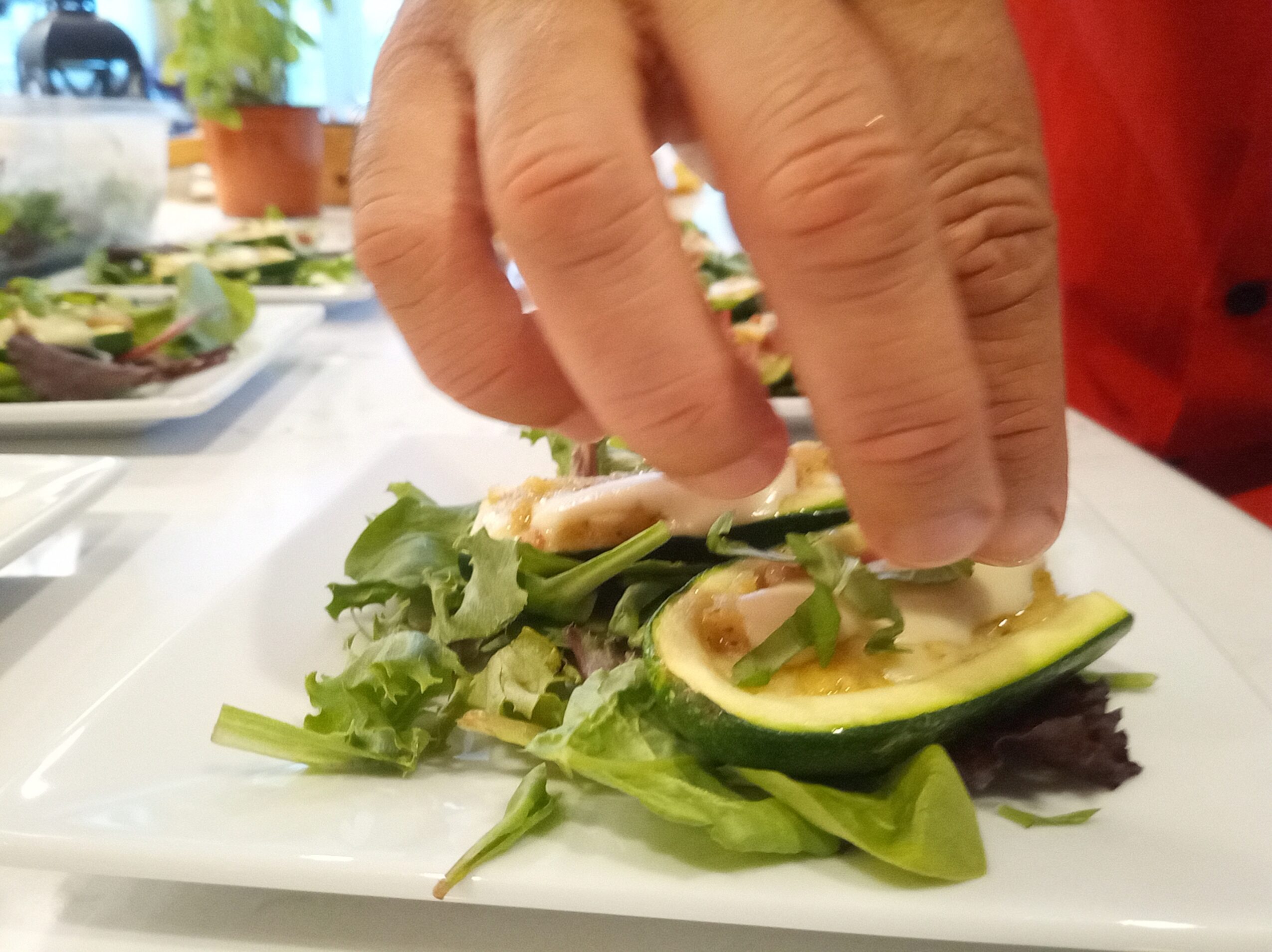 Hand placing sliced avocado and greens on a plate with salad ingredients, close-up view.