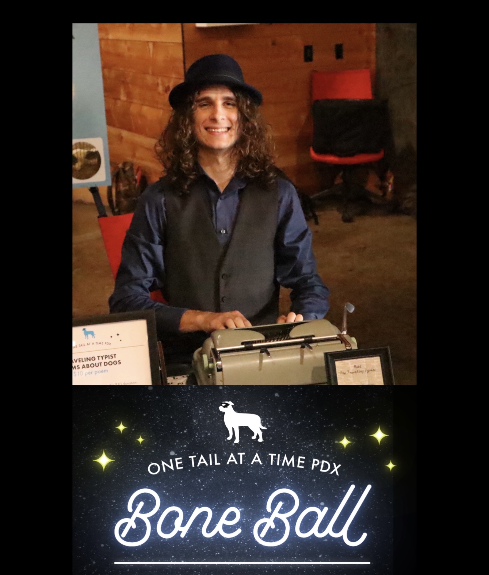 Person with curly hair wearing a hat and vest, smiling, sitting at a table with a typewriter, wooden background.