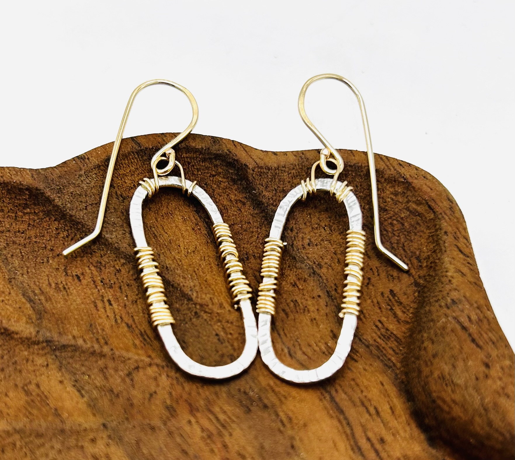 Gold and silver earrings with oval shapes and small beads, placed on a wooden surface.
