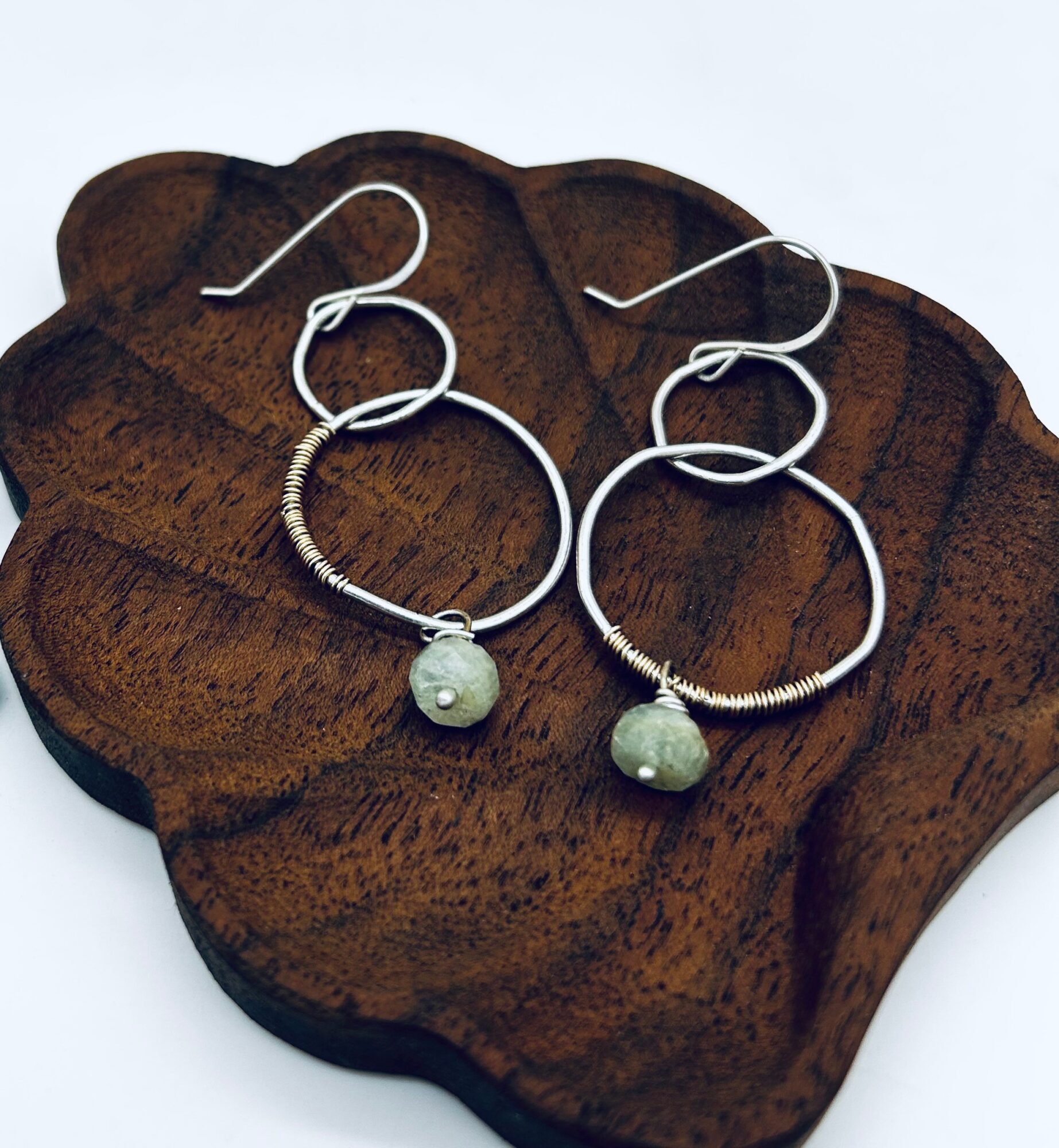 Pair of silver hoop earrings with round, light-colored beads, displayed on a wooden surface.