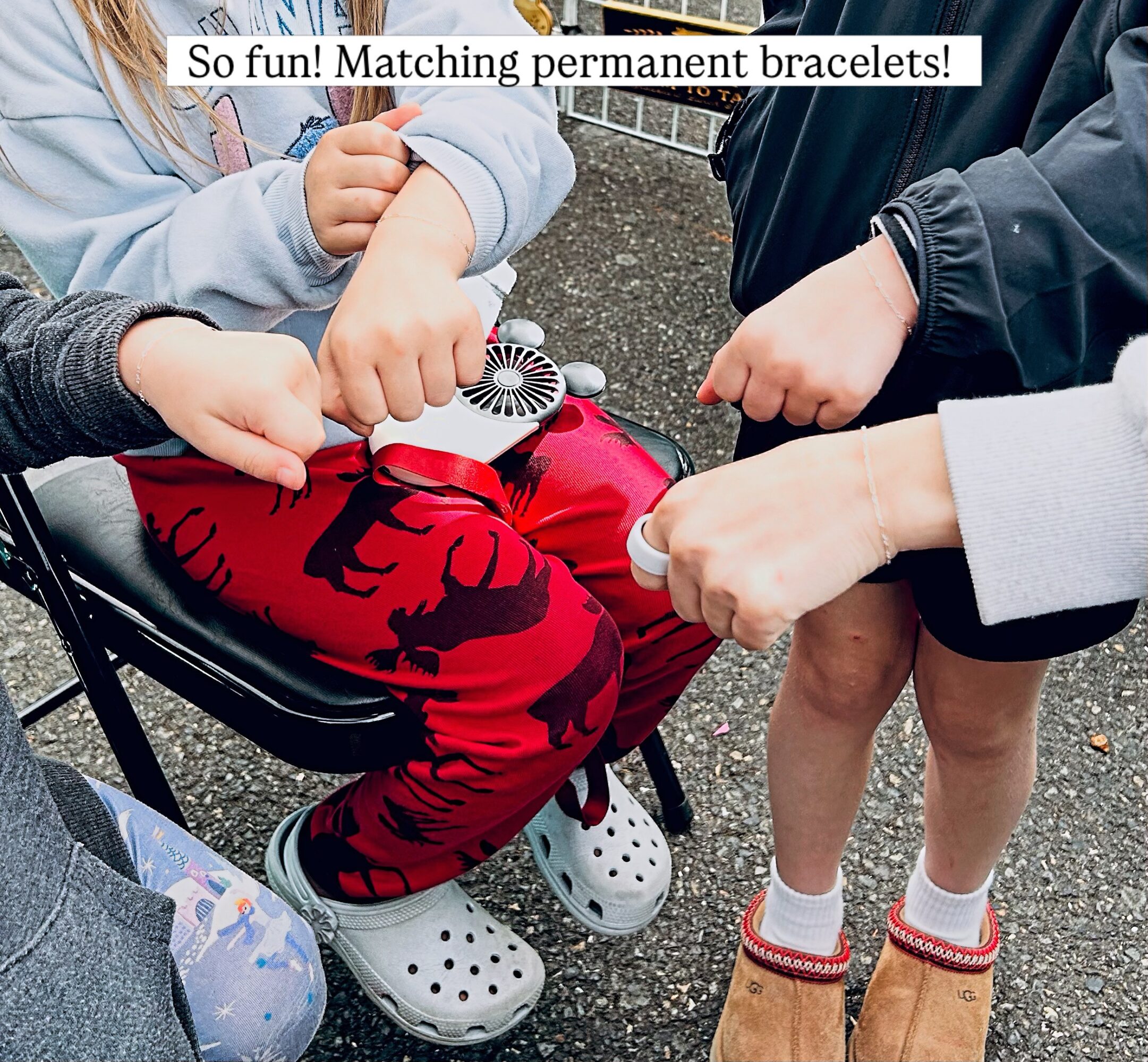 Children's hands showing matching bracelets, with a stroller and outdoor ground visible, celebrating friendship.