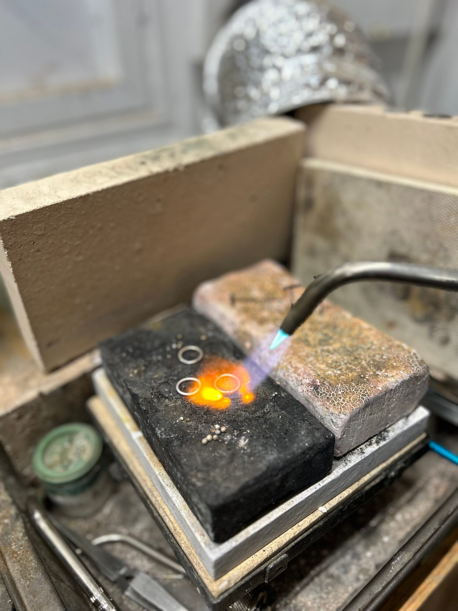 A soldering iron heats a circuit board with orange glow, surrounded by bricks and tools, in a workshop setting.