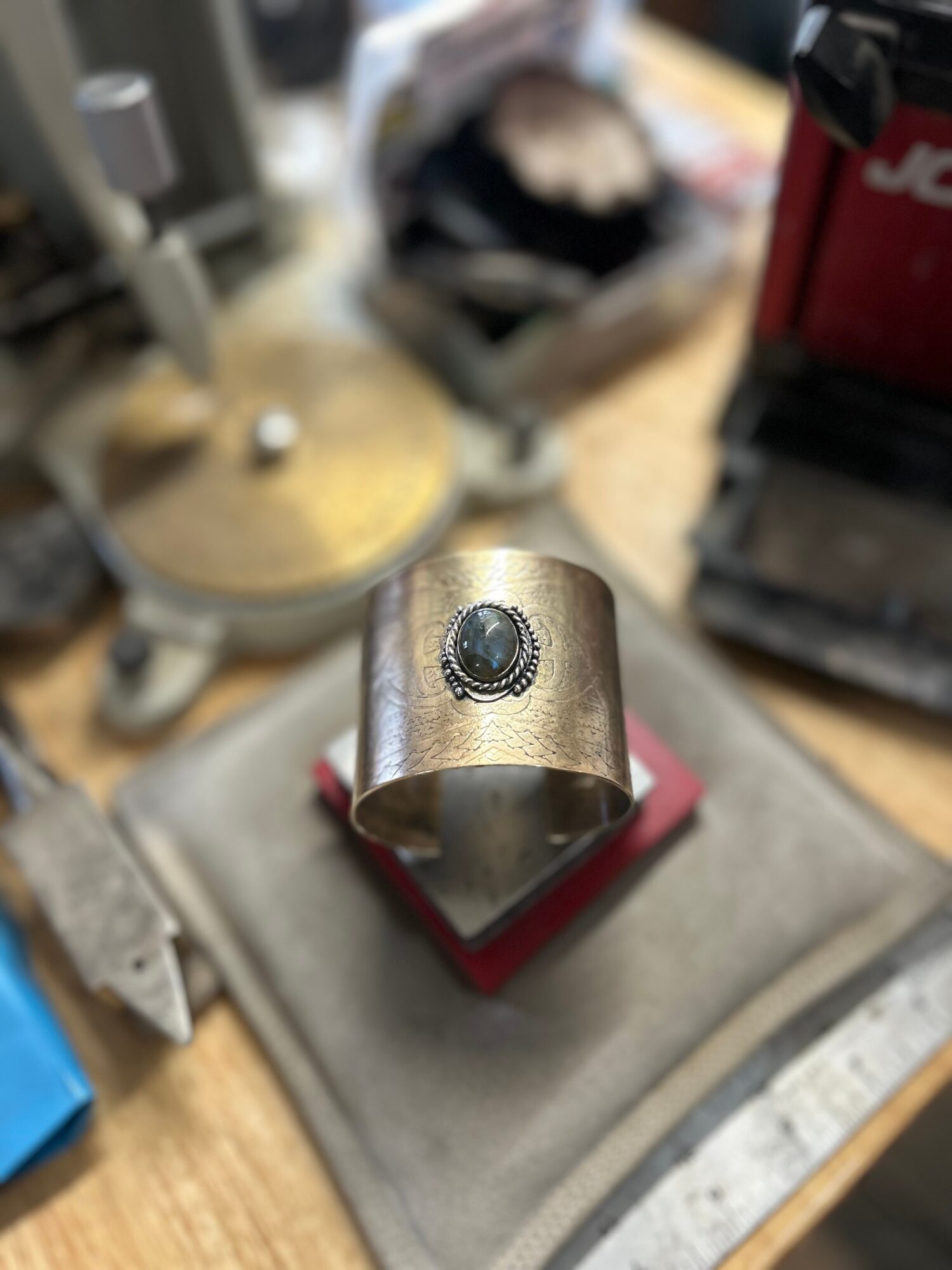 Metal ring with a black stone or button on top, placed on a red box on a workbench.