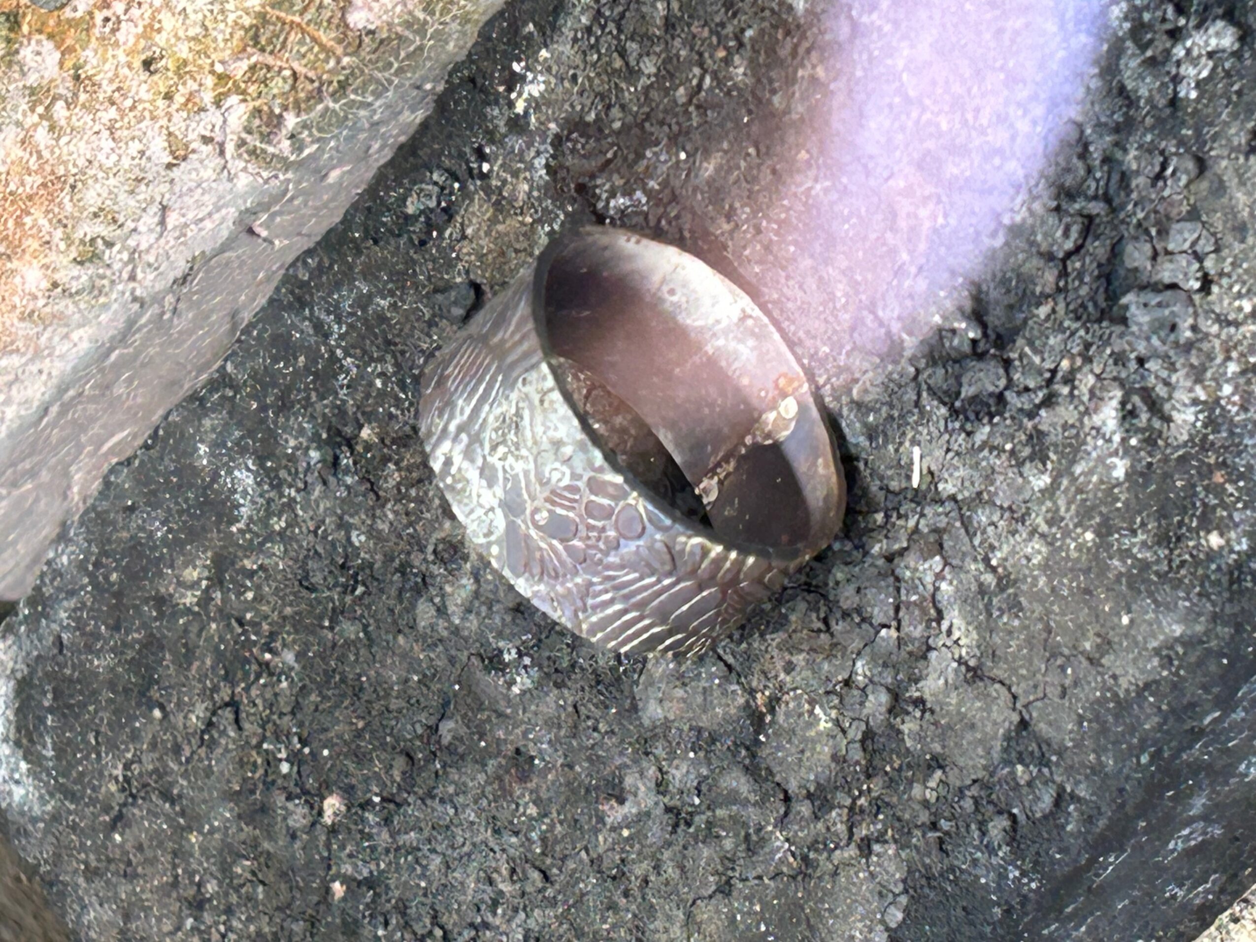 Metal pipe protrudes from ground with surrounding asphalt and dirt, partially covered in dirt and debris.