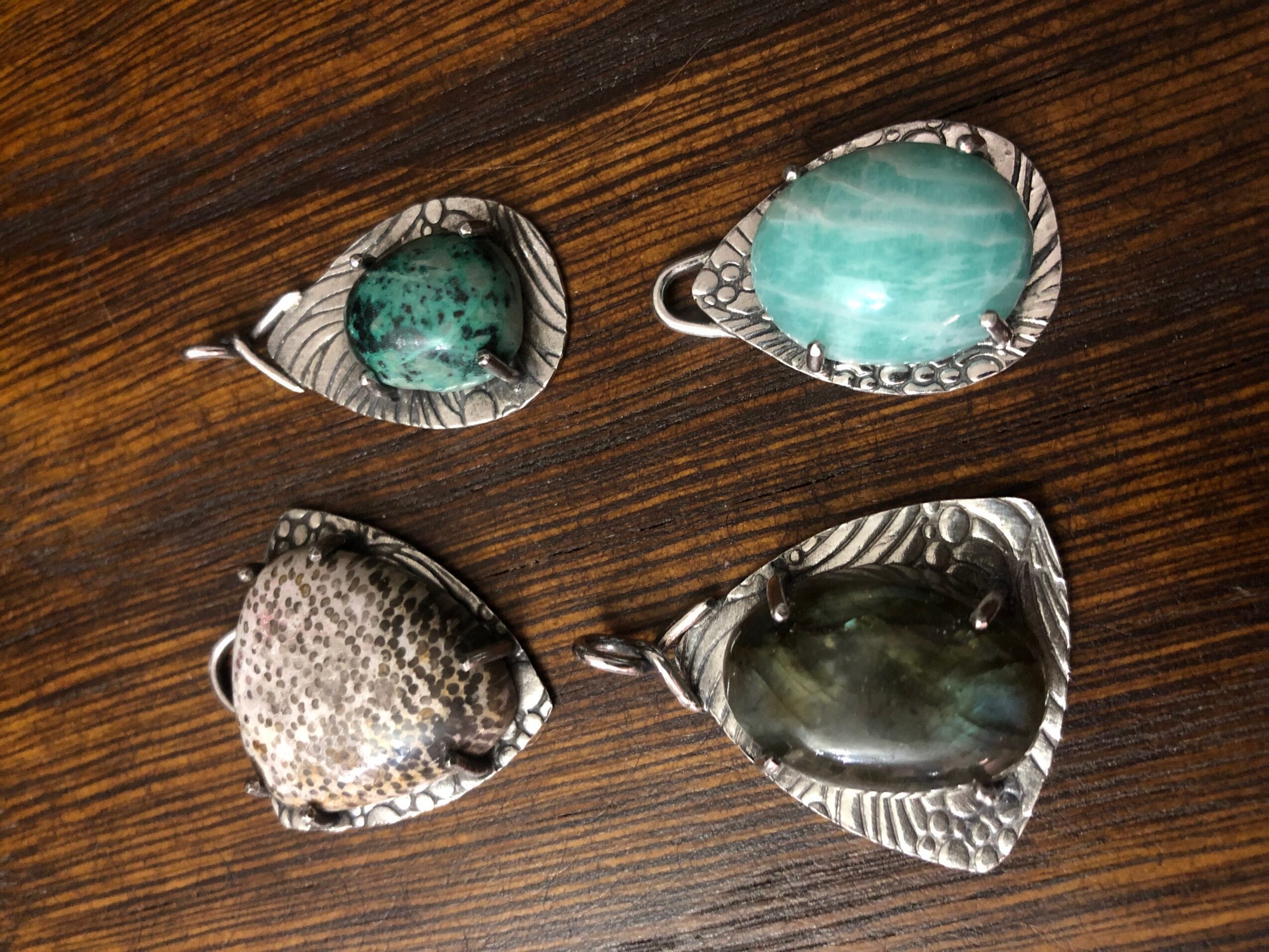 Four heart-shaped silver pendants with different stones on a wooden surface.