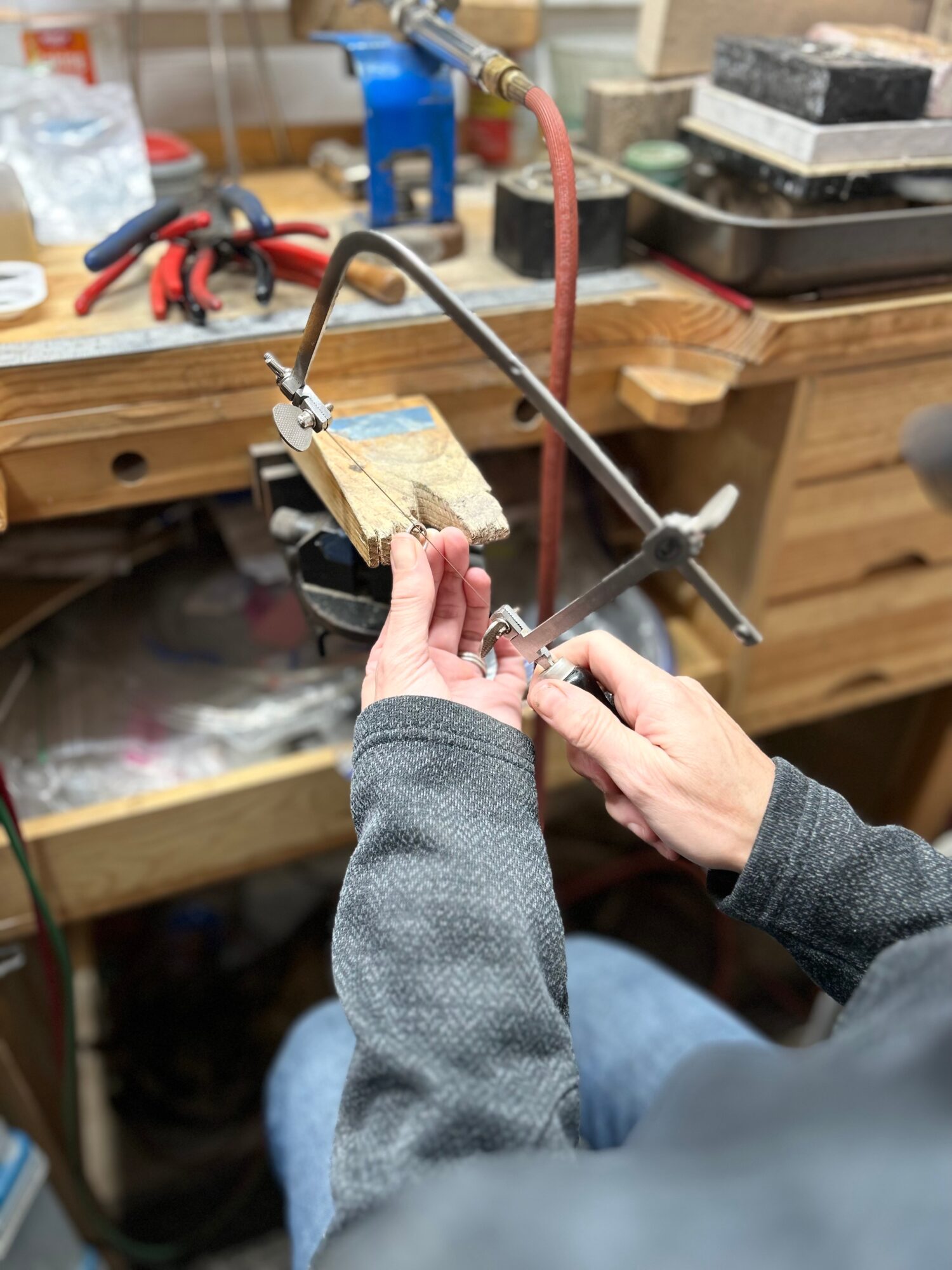 Person holding a small wooden piece in a workshop with tools and equipment in the background.