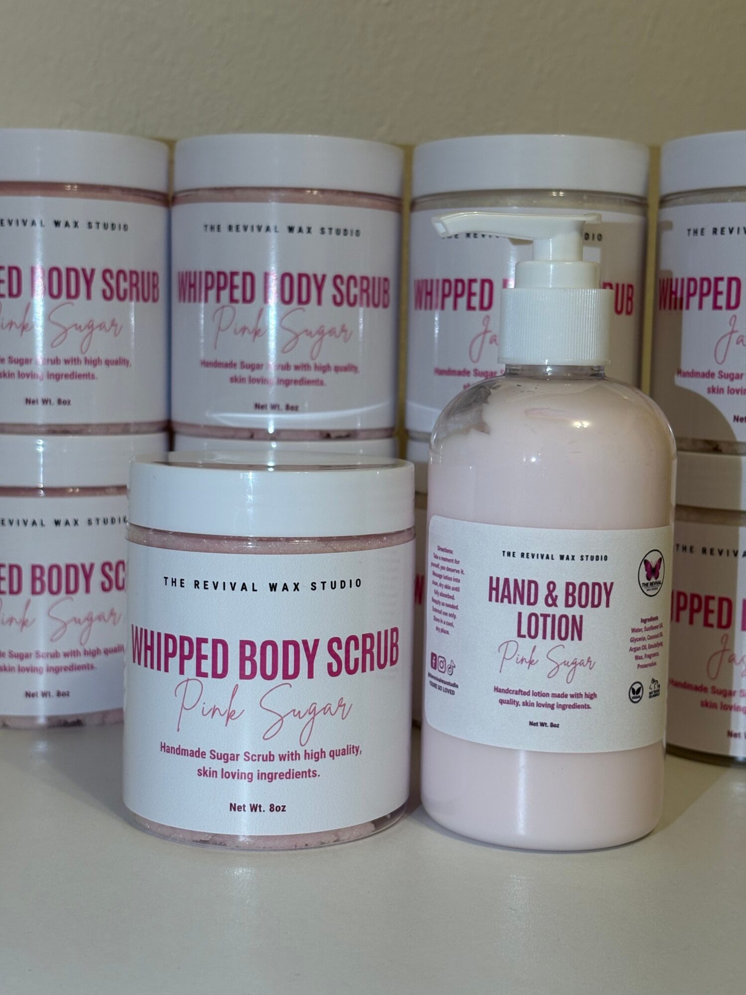 Four bottles of body scrub lotion stacked horizontally on a surface, with labels visible.