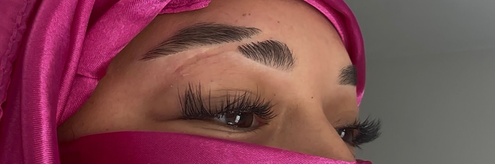 Close-up of a woman's face with makeup, eyes closed, wearing a pink headscarf.
