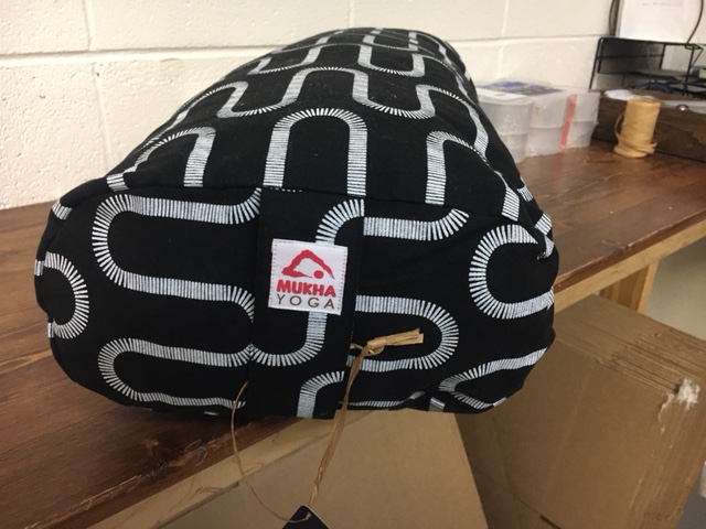 Black bag with white geometric pattern hanging from a string, with a cardboard box and wooden surface nearby.