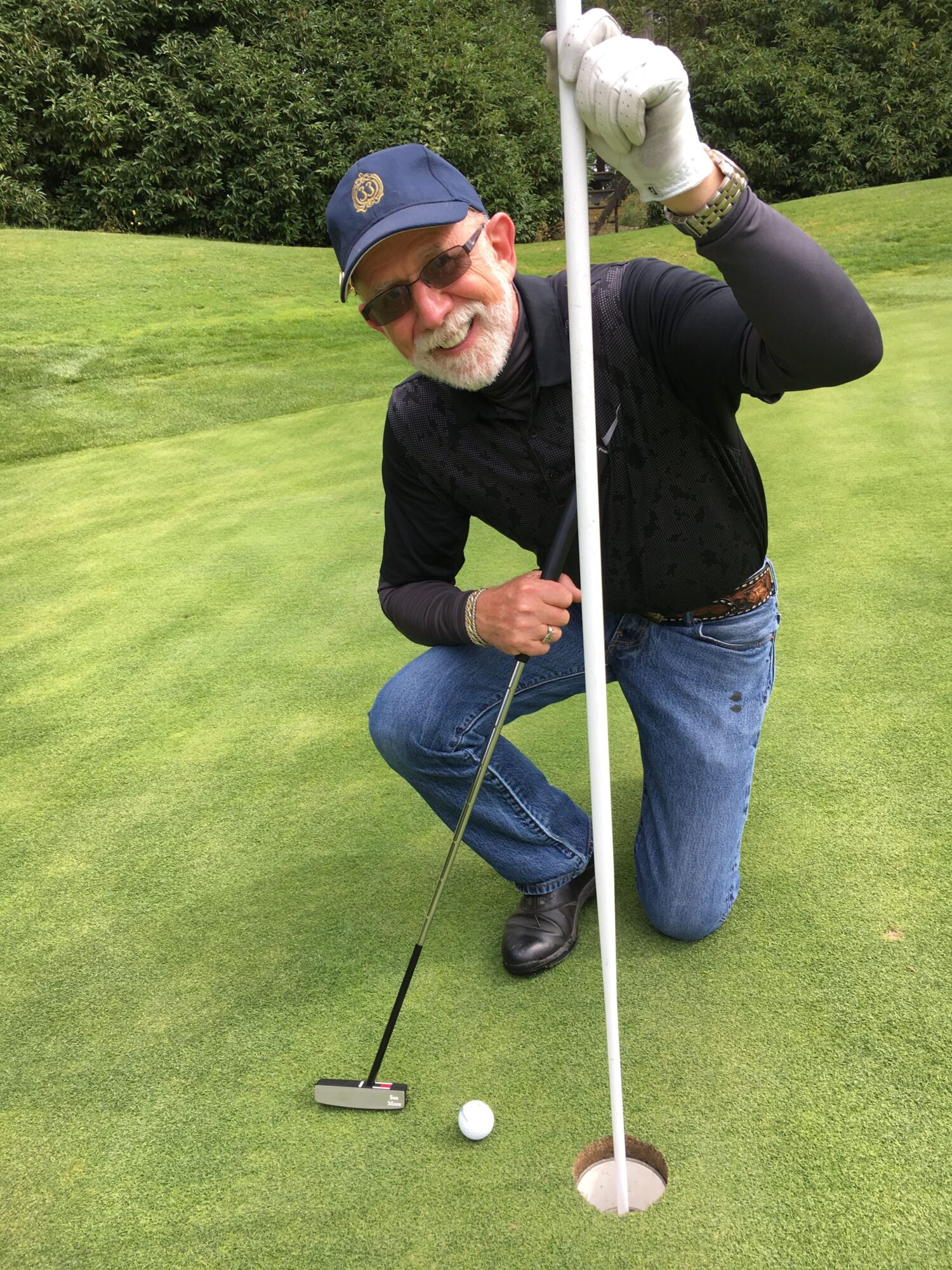 Person lying on grass holding a golf club, preparing to hit a golf ball, with a golf tee nearby.