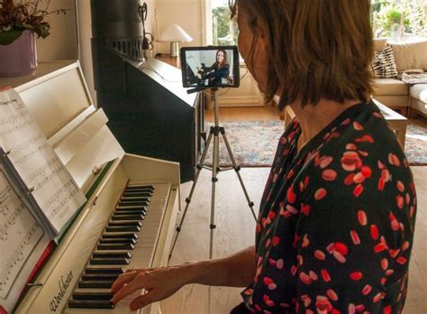 Woman playing piano while recording herself with a camera on a tripod in a living room.