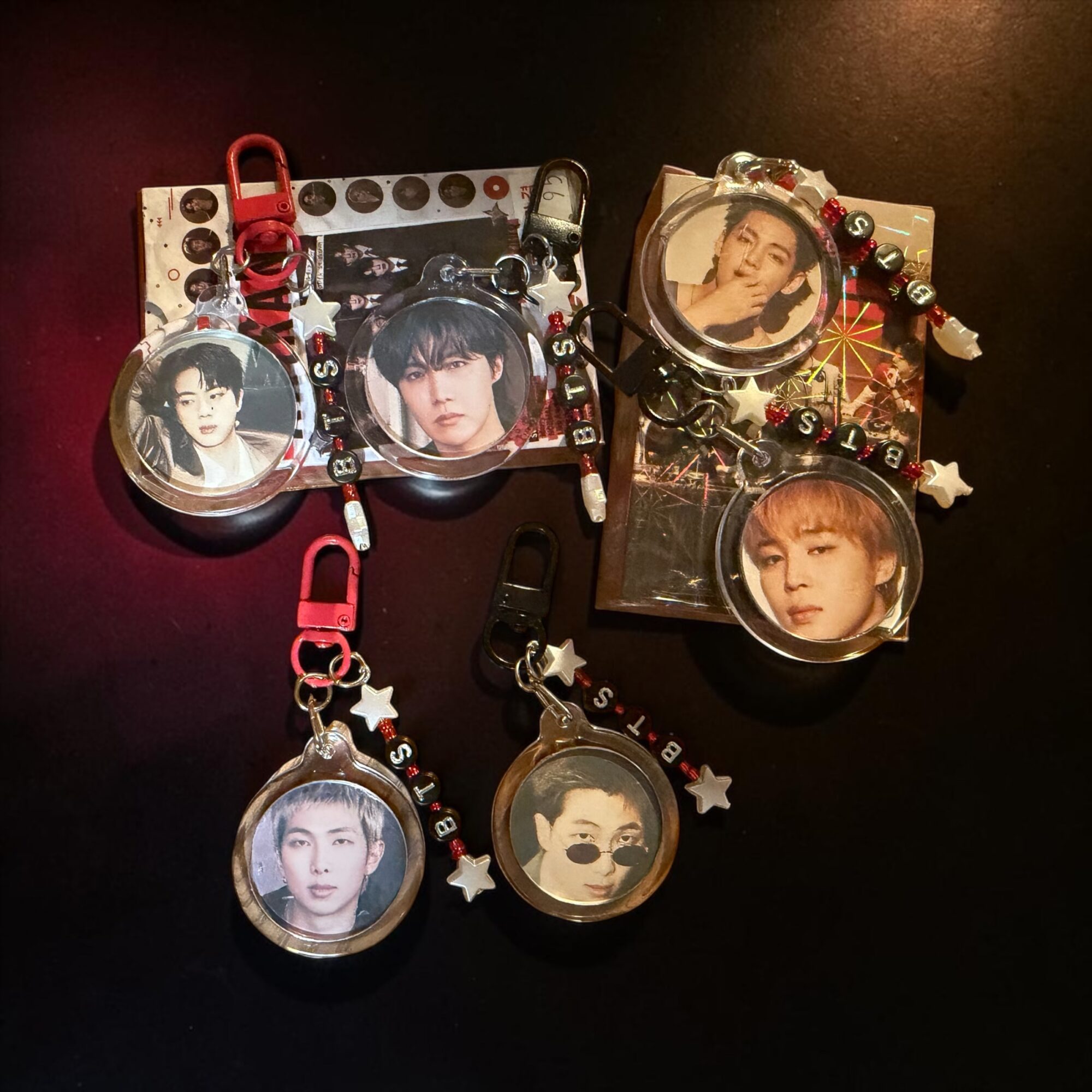 Collection of six circular keychains with photos of young men, decorated with stars and beads, on a dark surface.