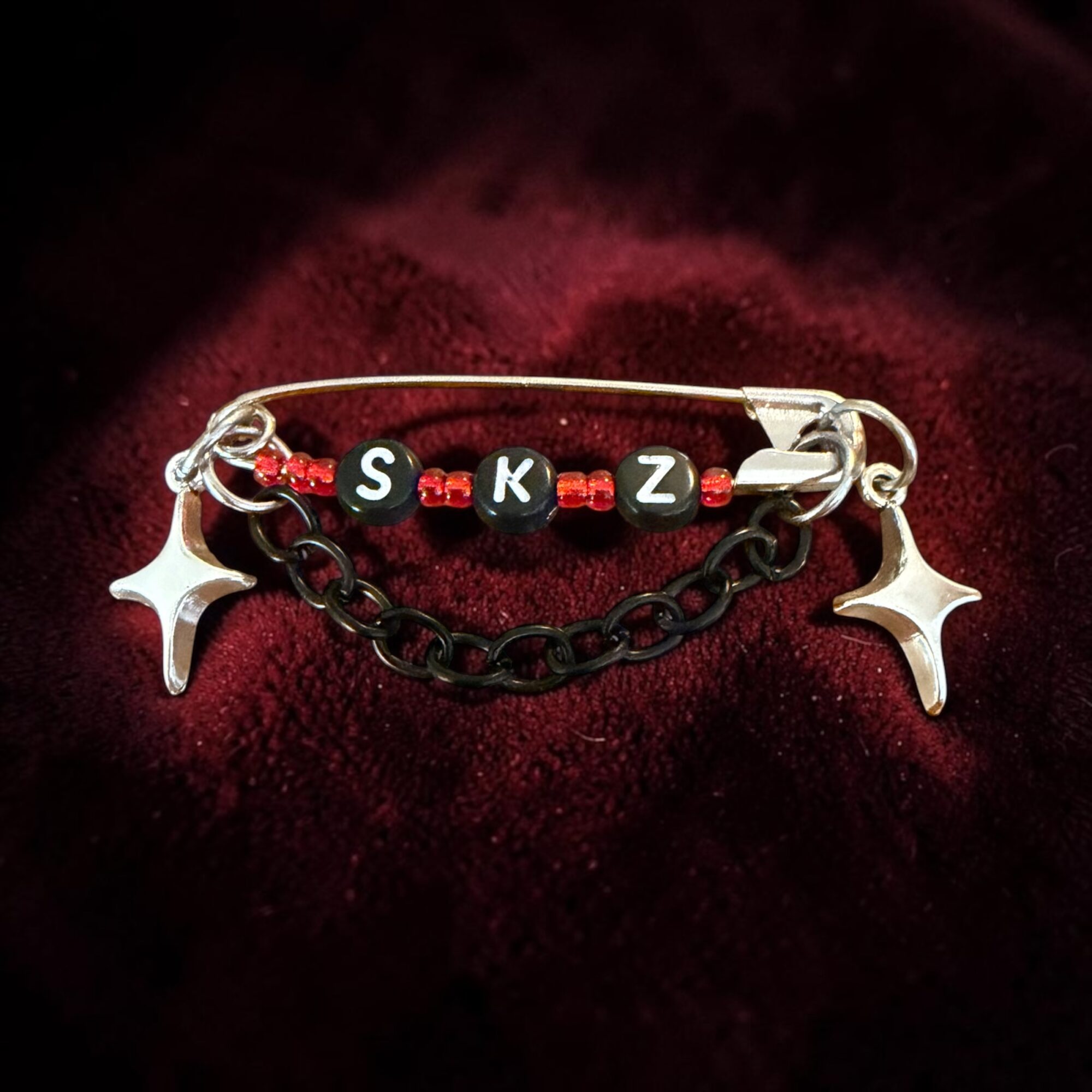 Beaded bracelet with black and red beads, silver star charms, and a chain, on a dark red fabric background.