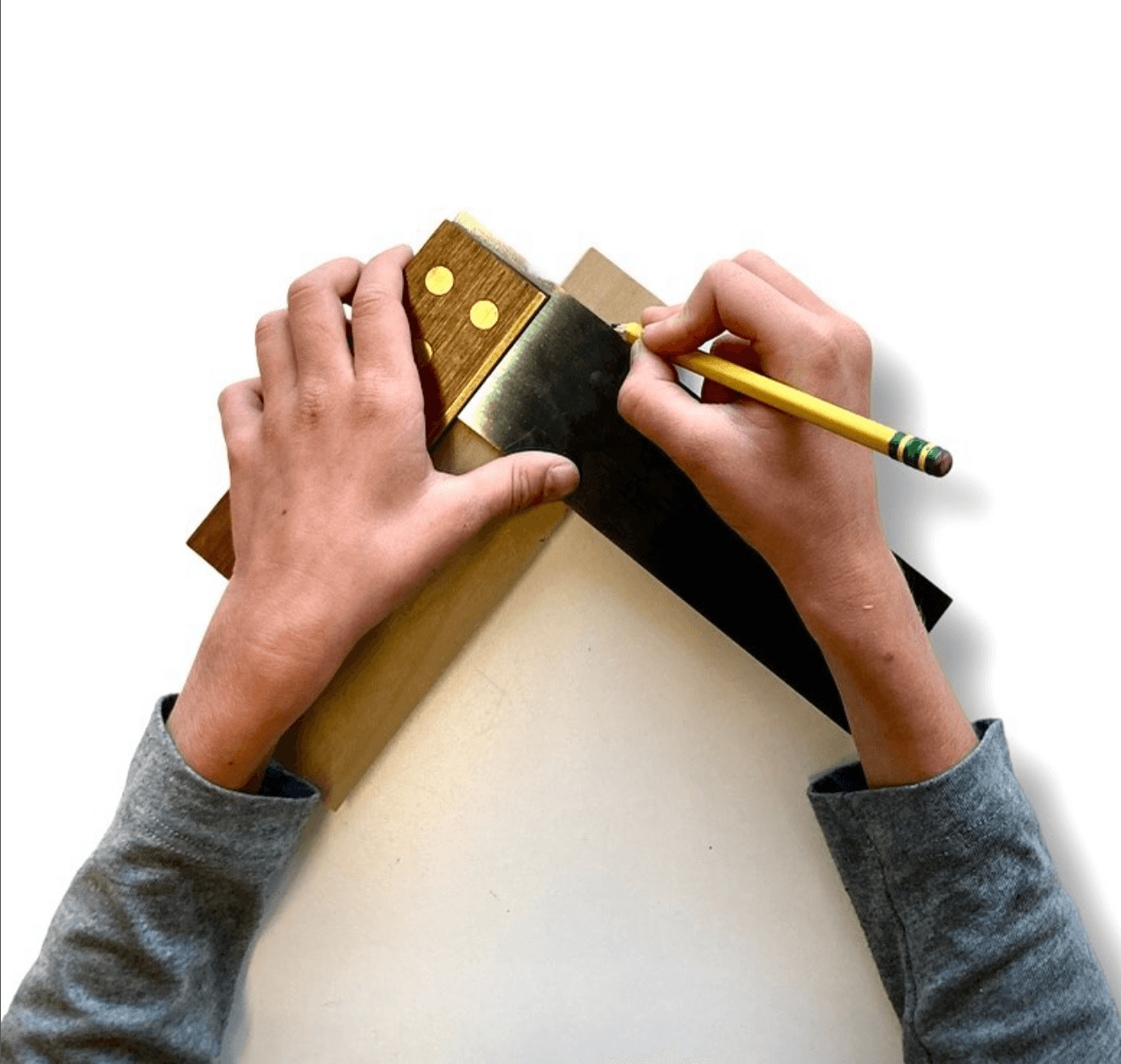 Person's hands using a metal square and pencil to draw on a piece of paper, with a white background.