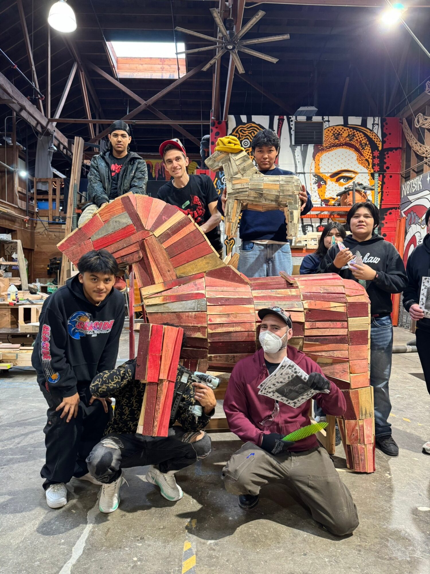 Group of people with a large, colorful, abstract sculpture in an indoor space with artwork and structures in the background.
