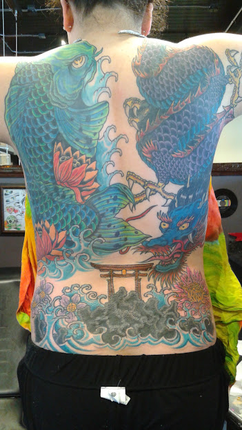 Back tattoo of two large, colorful dragons facing each other with waves and clouds, and a bridge below.