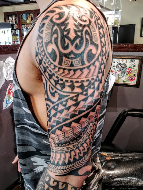 Detailed tribal tattoo covers upper arm and shoulder with geometric and abstract patterns.