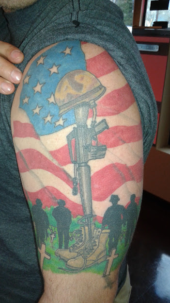 Tattoo of a soldier's silhouette, American flag background, moon, and stars, with two figures at the bottom, on upper arm.