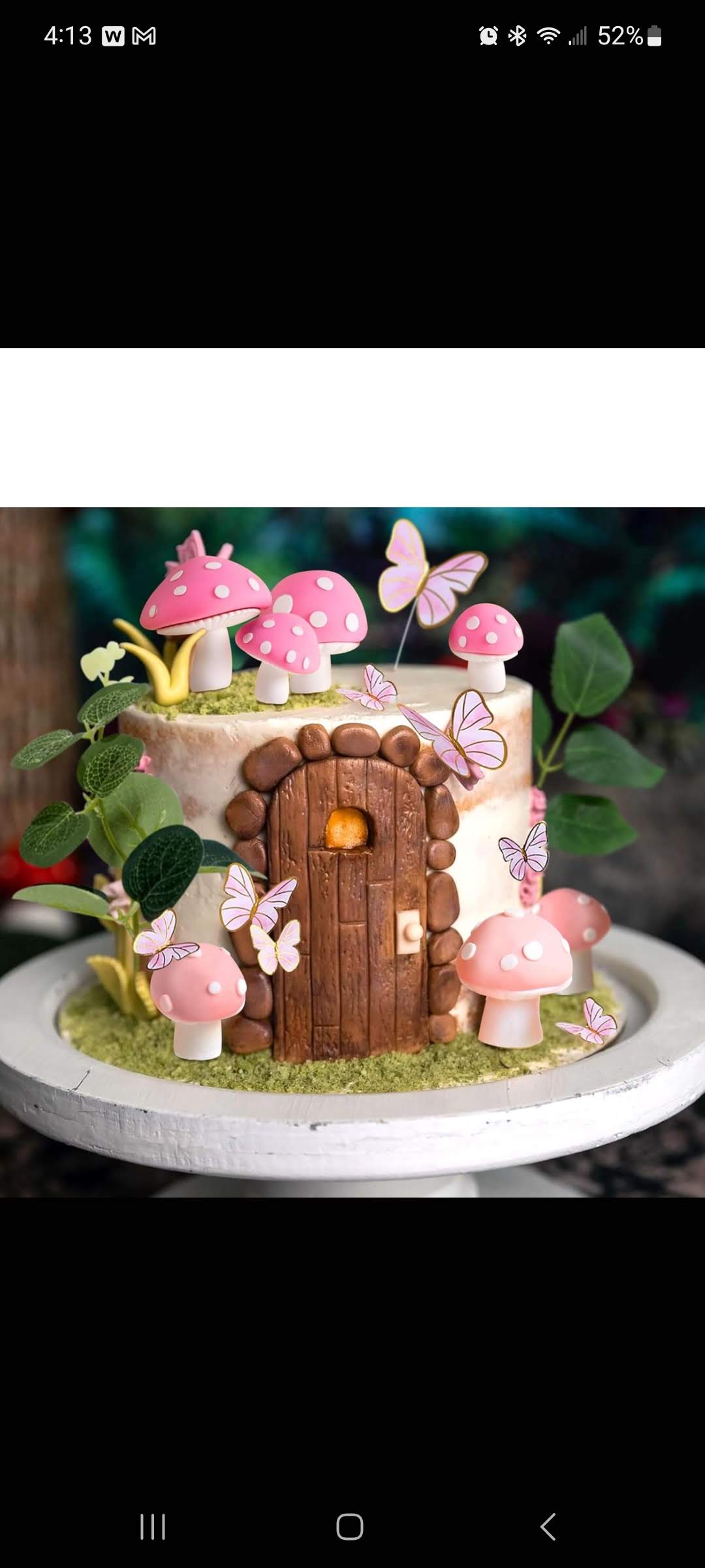 Decorative fairy house with pink mushrooms, butterflies, and greenery on a white base, whimsical and colorful.