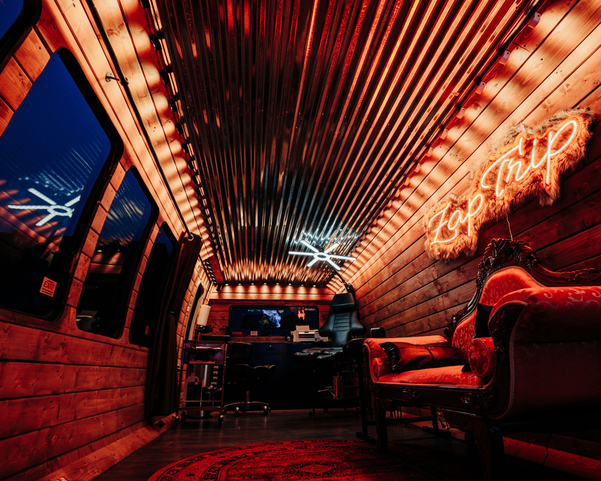 Interior of a cozy lounge with wooden walls, neon sign, and seating area, illuminated by warm lighting.