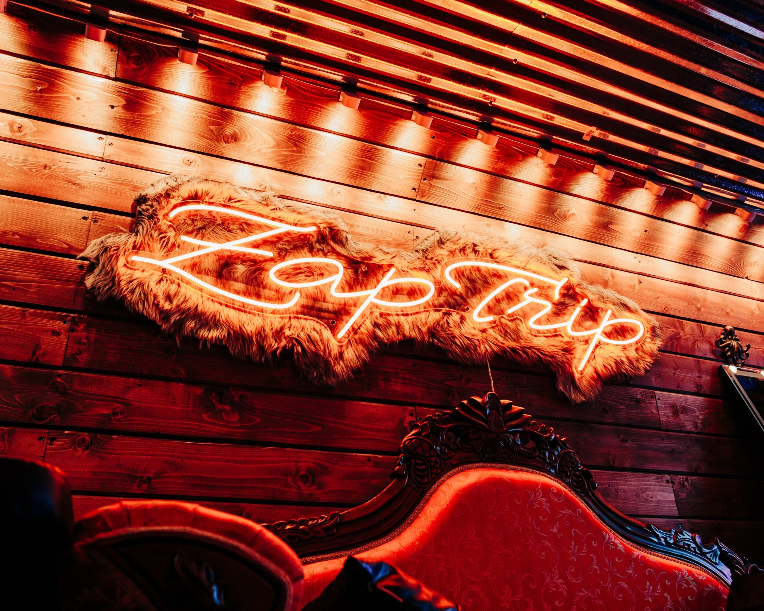 Neon sign reading 'Happy' on a wooden wall with warm lighting, decorative fur trim, and a red upholstered chair.
