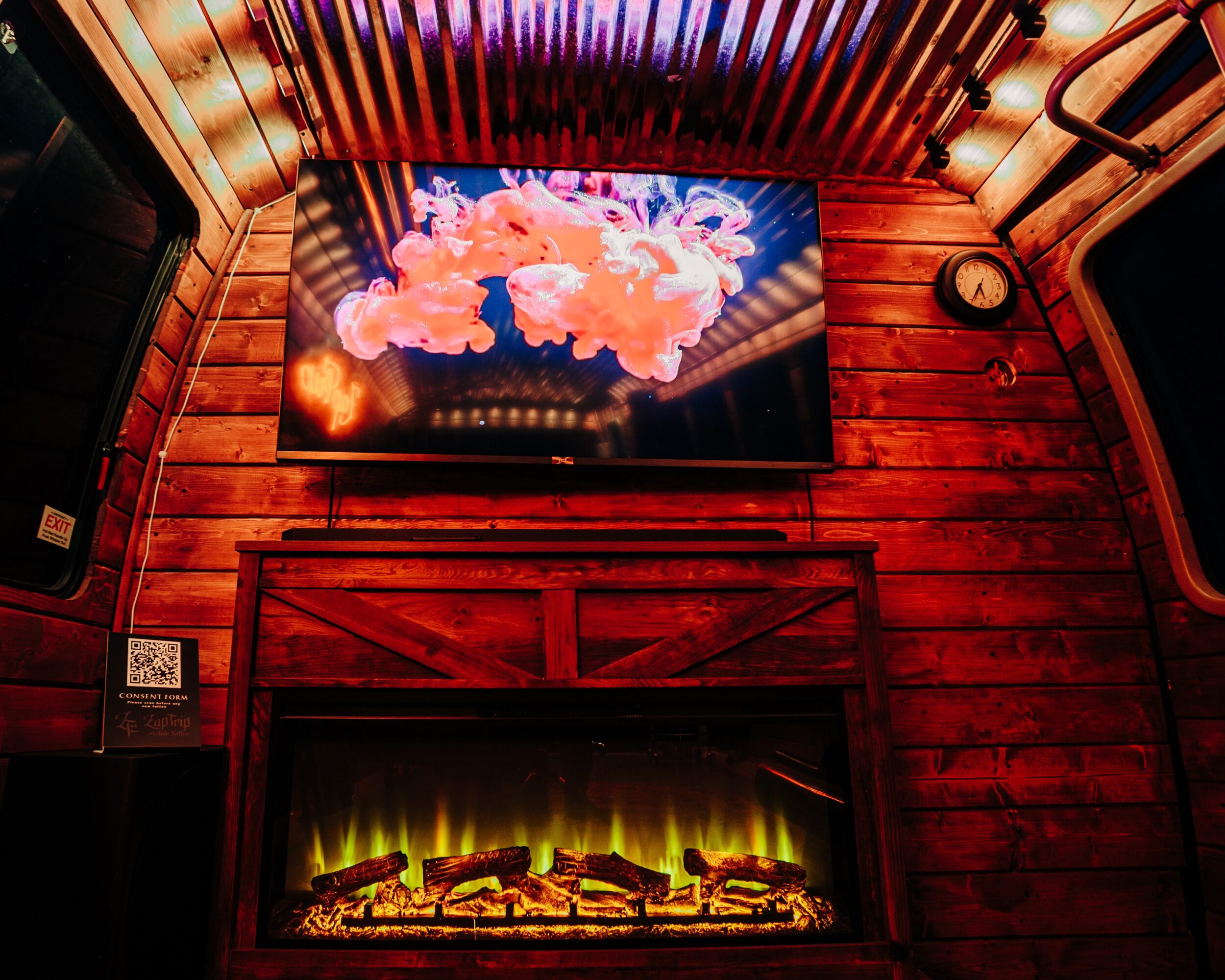 Wood-paneled wall with a large screen displaying colorful clouds and a fireplace below with glowing logs.