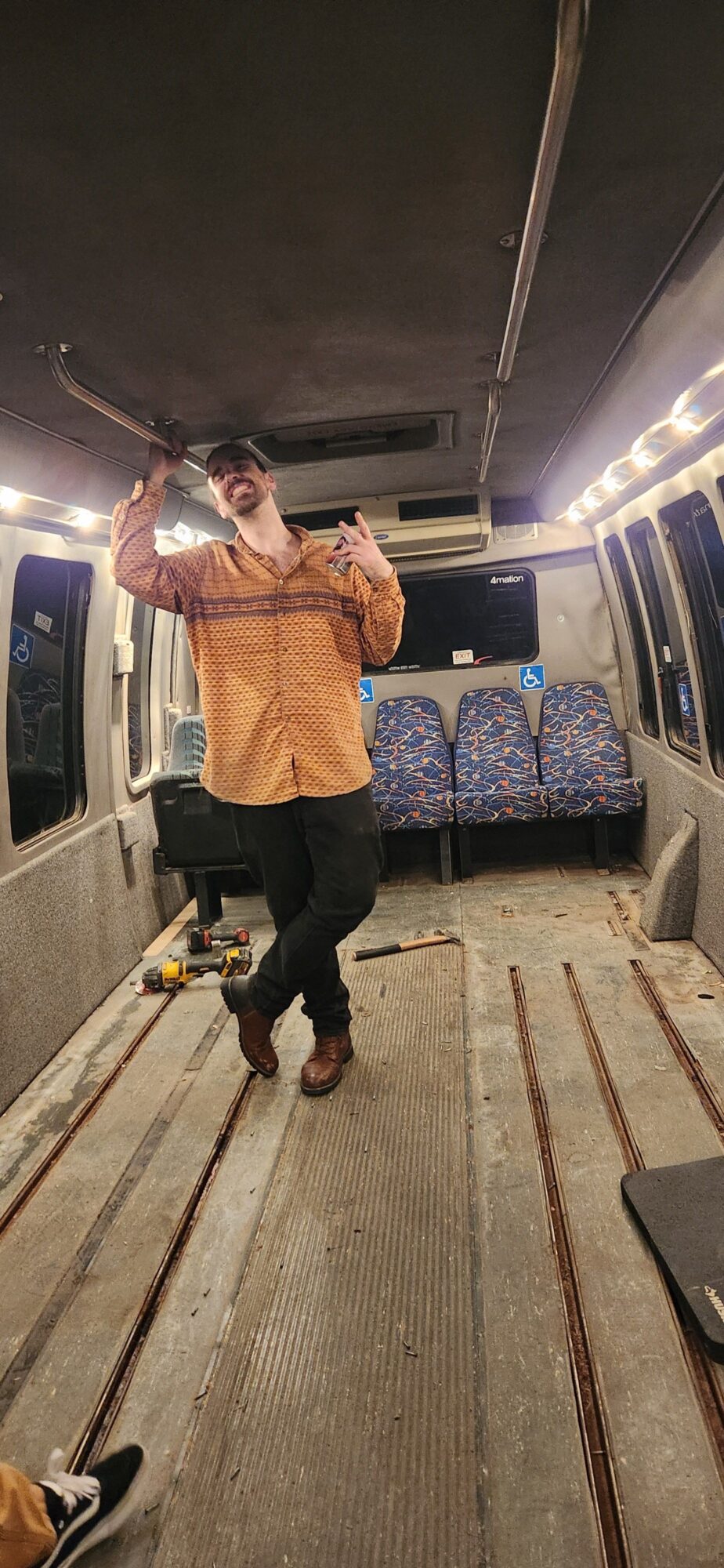 Person standing inside a train, holding a phone, with seats and tracks visible. The image is rotated 90 degrees clockwise.