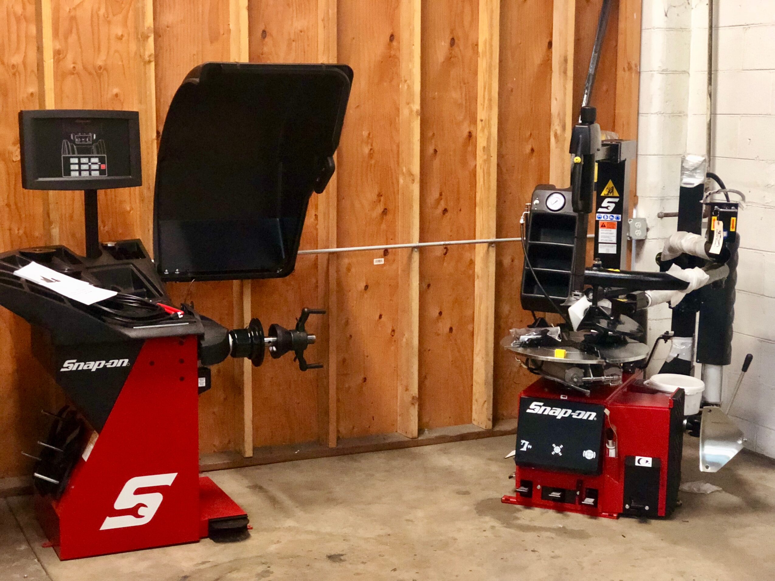 Workshop with a red and black Snap-on machine, a black chair, and tools against a wooden wall.