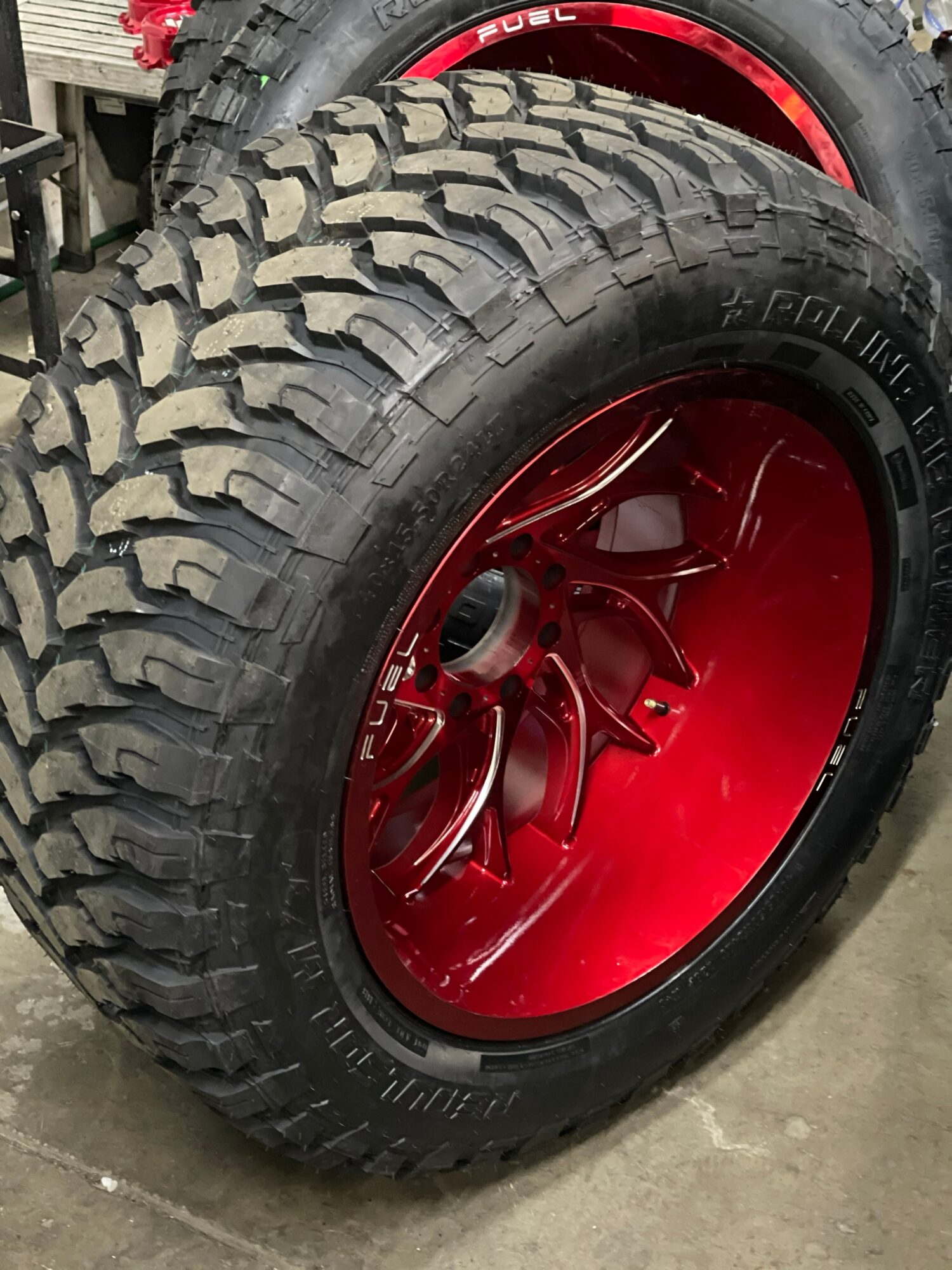 Close-up of a tire with a red rim and rugged tread pattern, leaning against another tire with a similar rim.