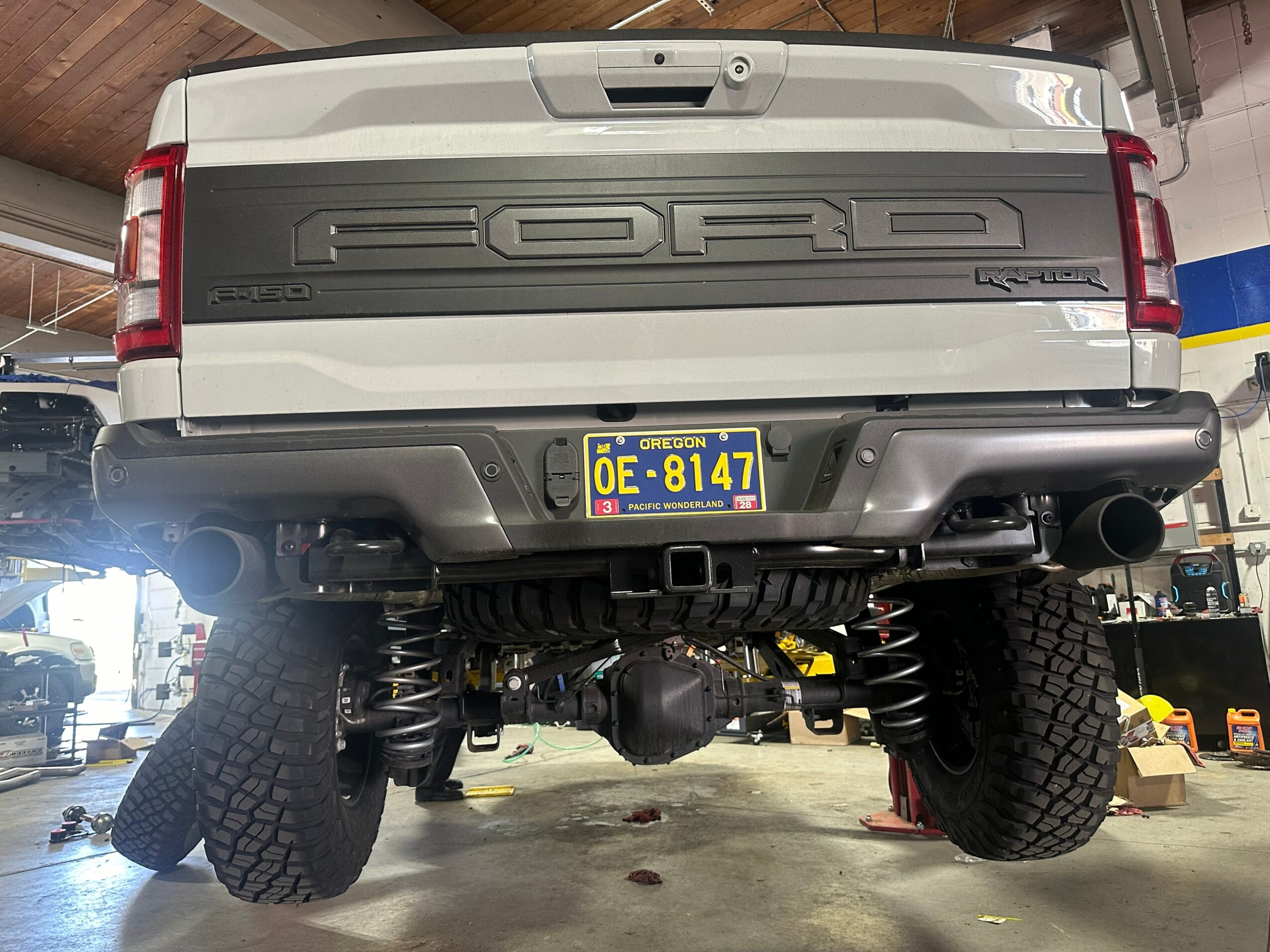 Rear view of a pickup truck with large tires, lifted suspension, and a yellow license plate, inside a garage.