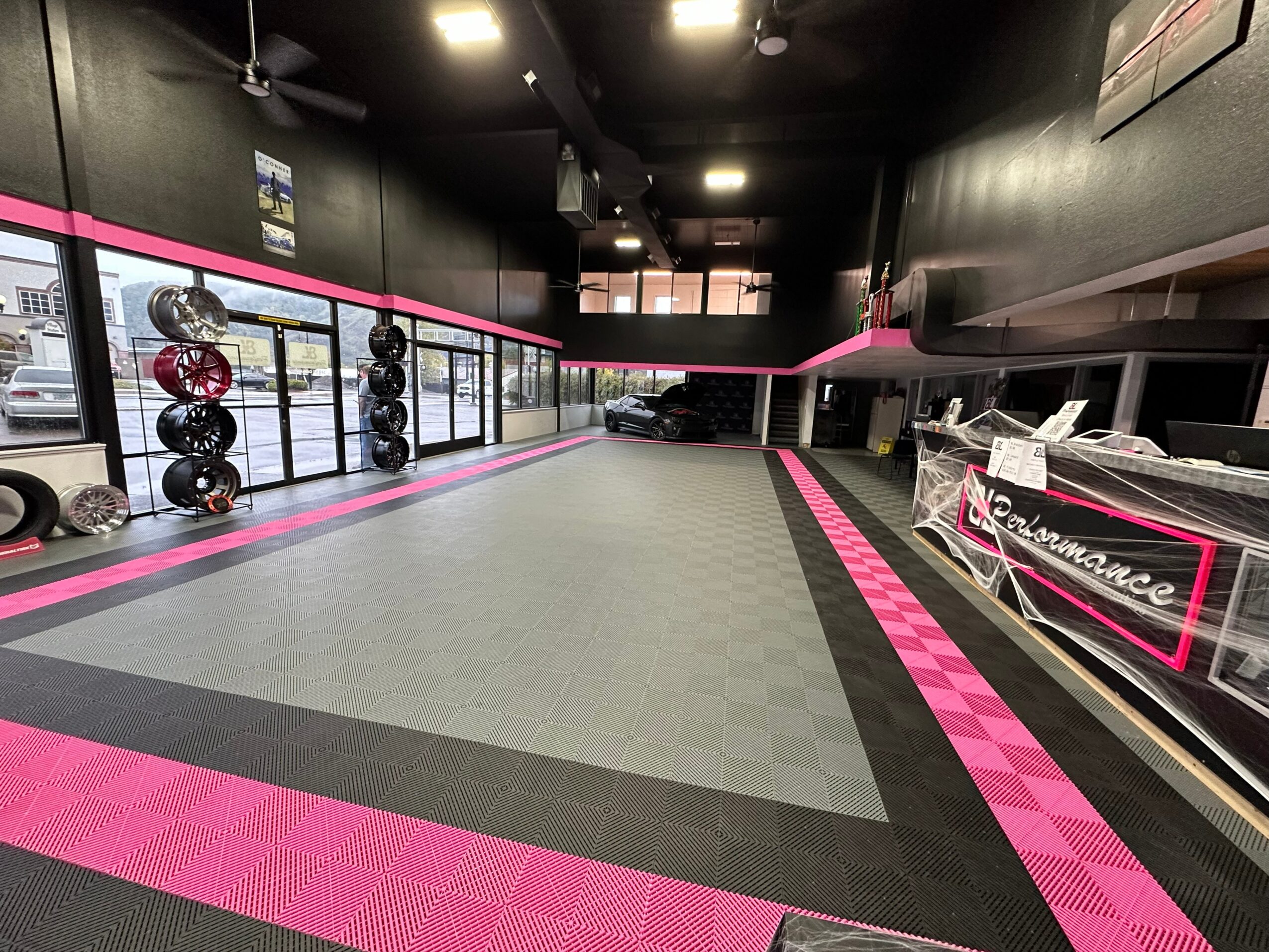 Empty gym with black walls, pink accents, and exercise equipment along the walls, large open space in the center.