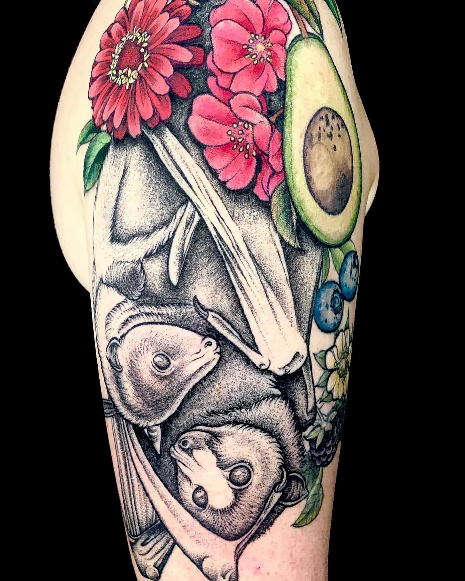 Tattoo of pink flowers, an avocado, blueberries, and two small animals on a person's arm.