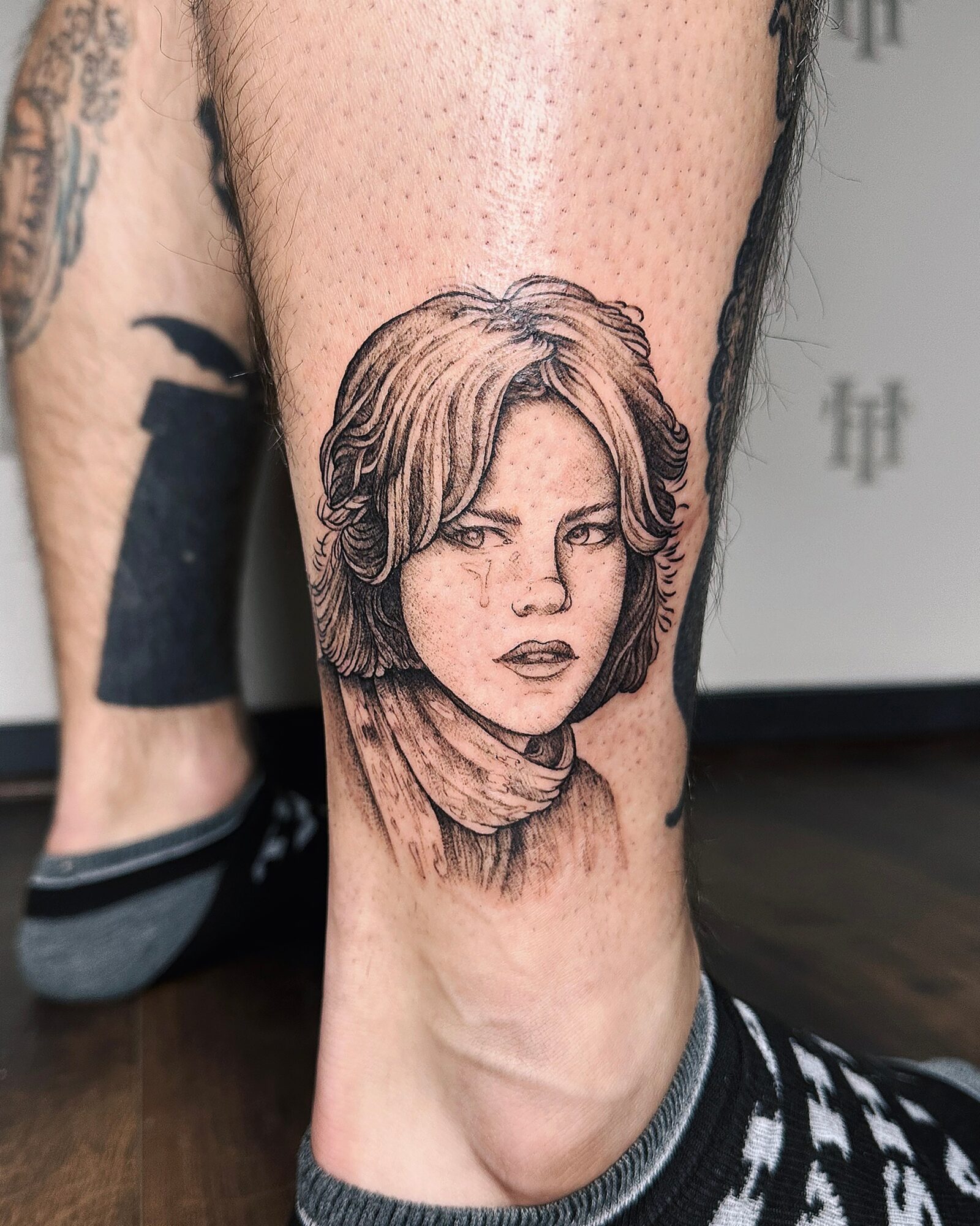 Tattoo of a woman's face with short hair on person's leg, with a neutral background.
