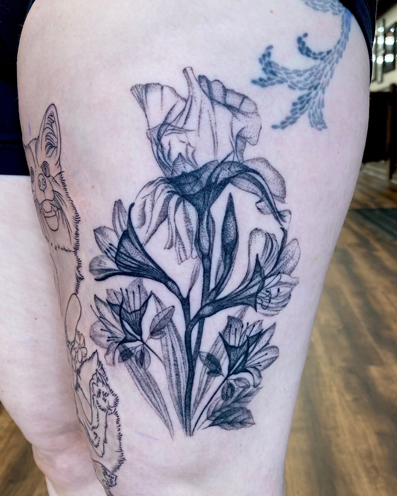 Tattoo of a detailed flower with leaves on person's thigh, with other tattoos visible nearby.