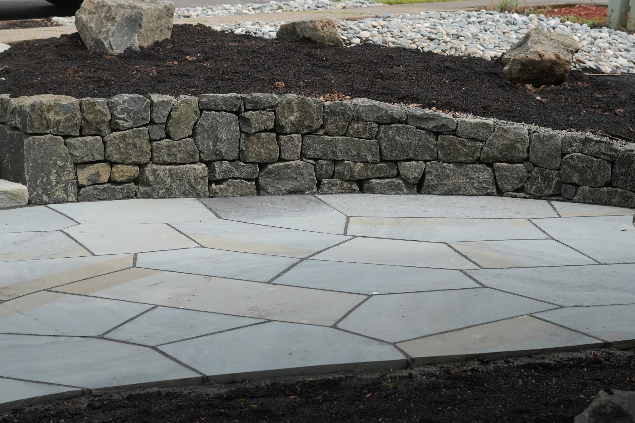 Stone pathway with a curved stone wall and soil in the background.