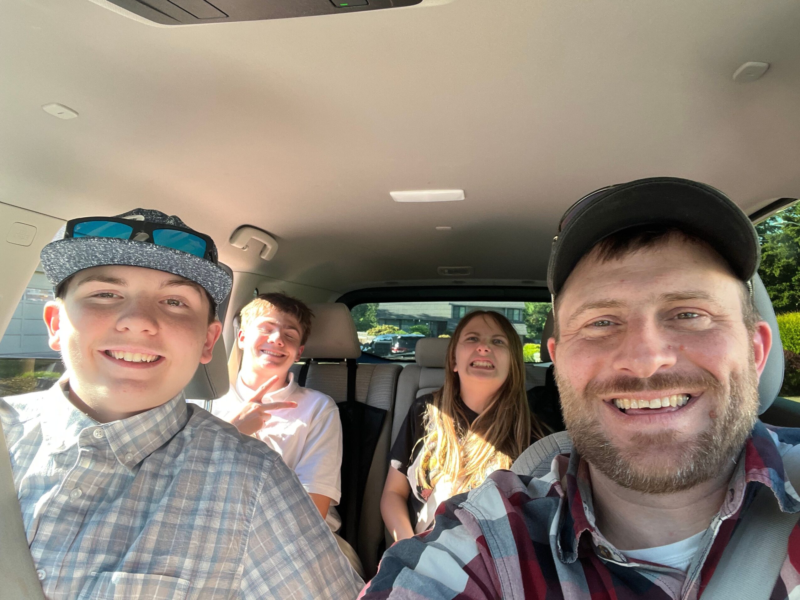 Four people inside a vehicle, smiling and taking a selfie, with trees visible outside the windows.