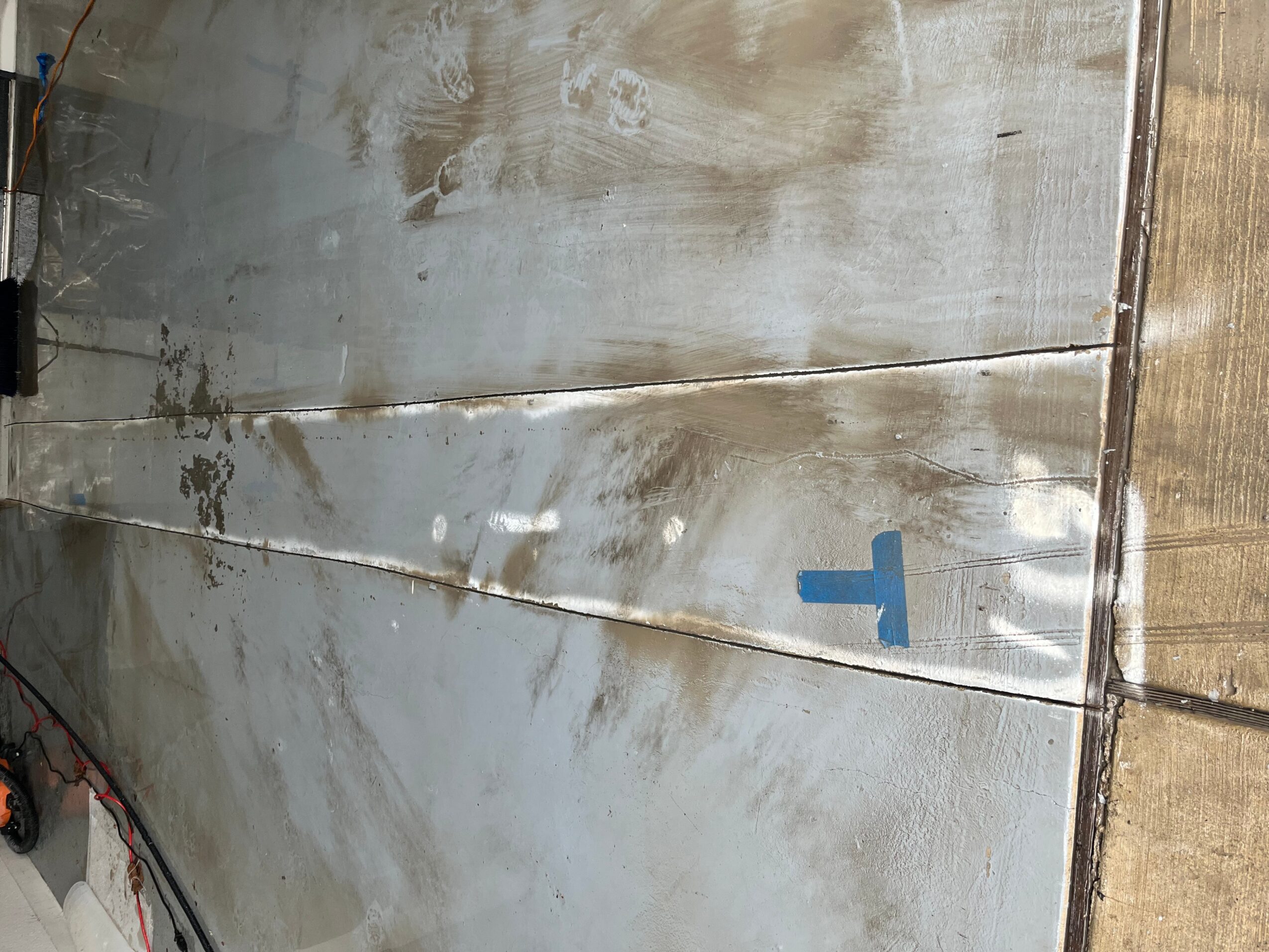 Metal surface with reflections and a blue letter T, partially visible, with wooden edge on the right.