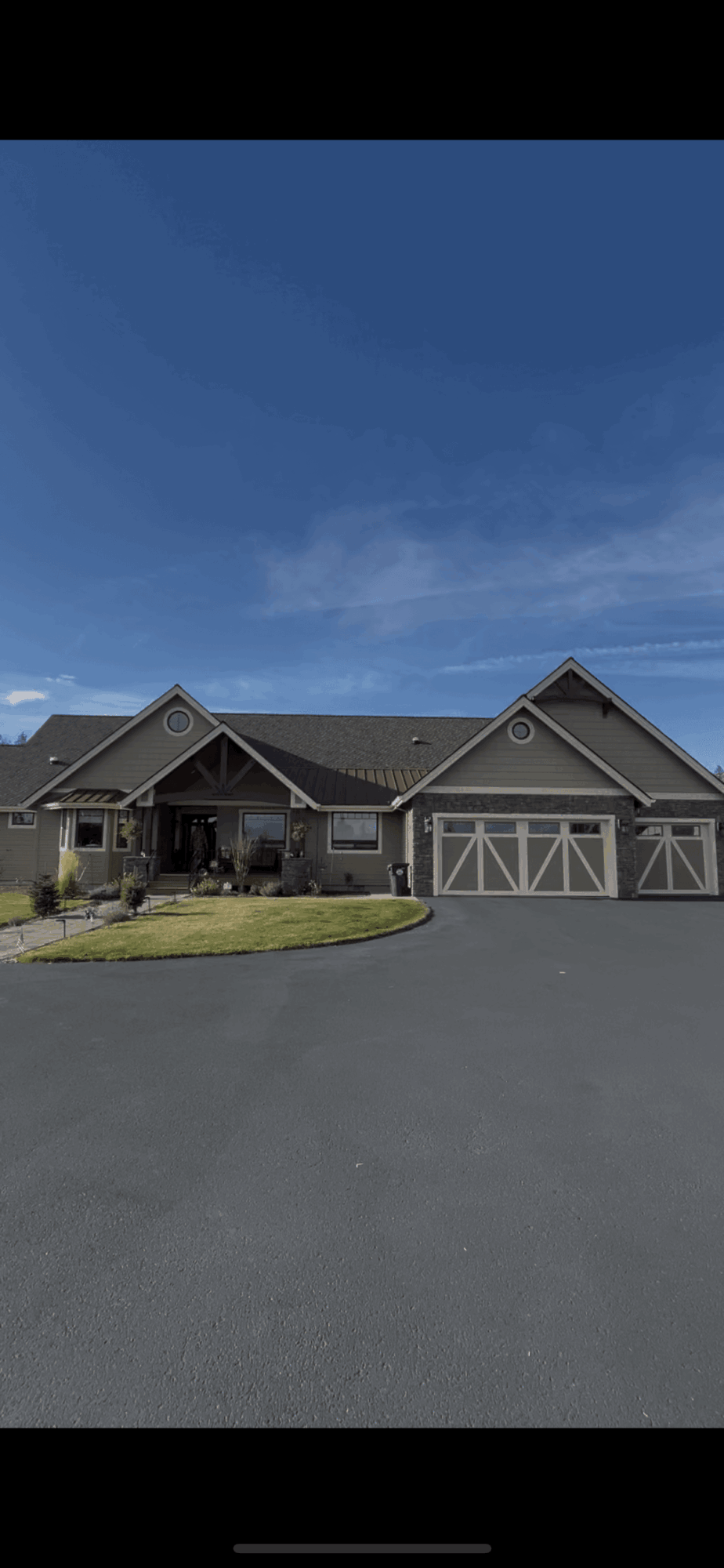 Single-story house with a large driveway, garage, and a front lawn under a blue sky.