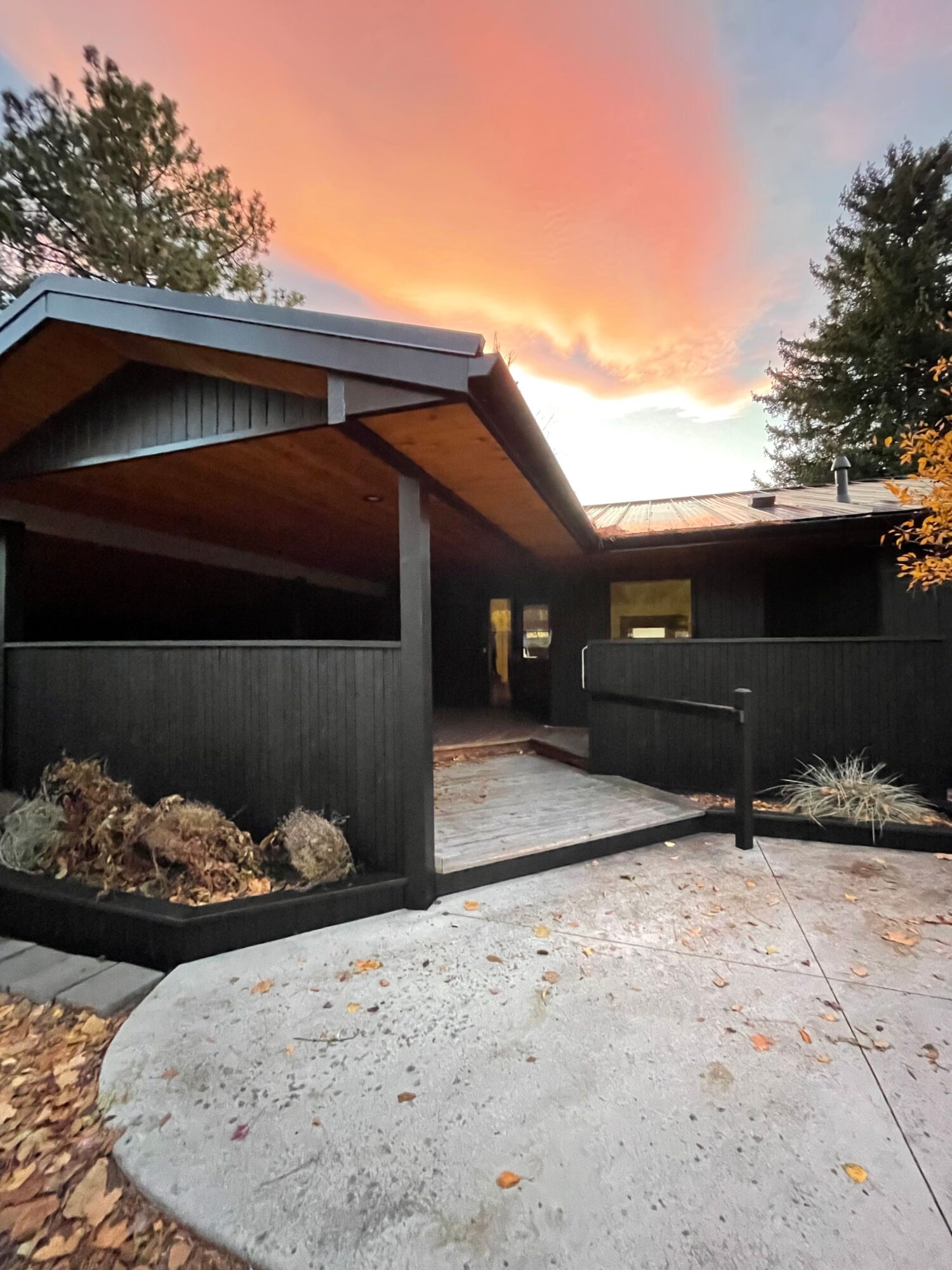 Black house with wooden interior, outdoor patio, and sunset sky with pink clouds.
