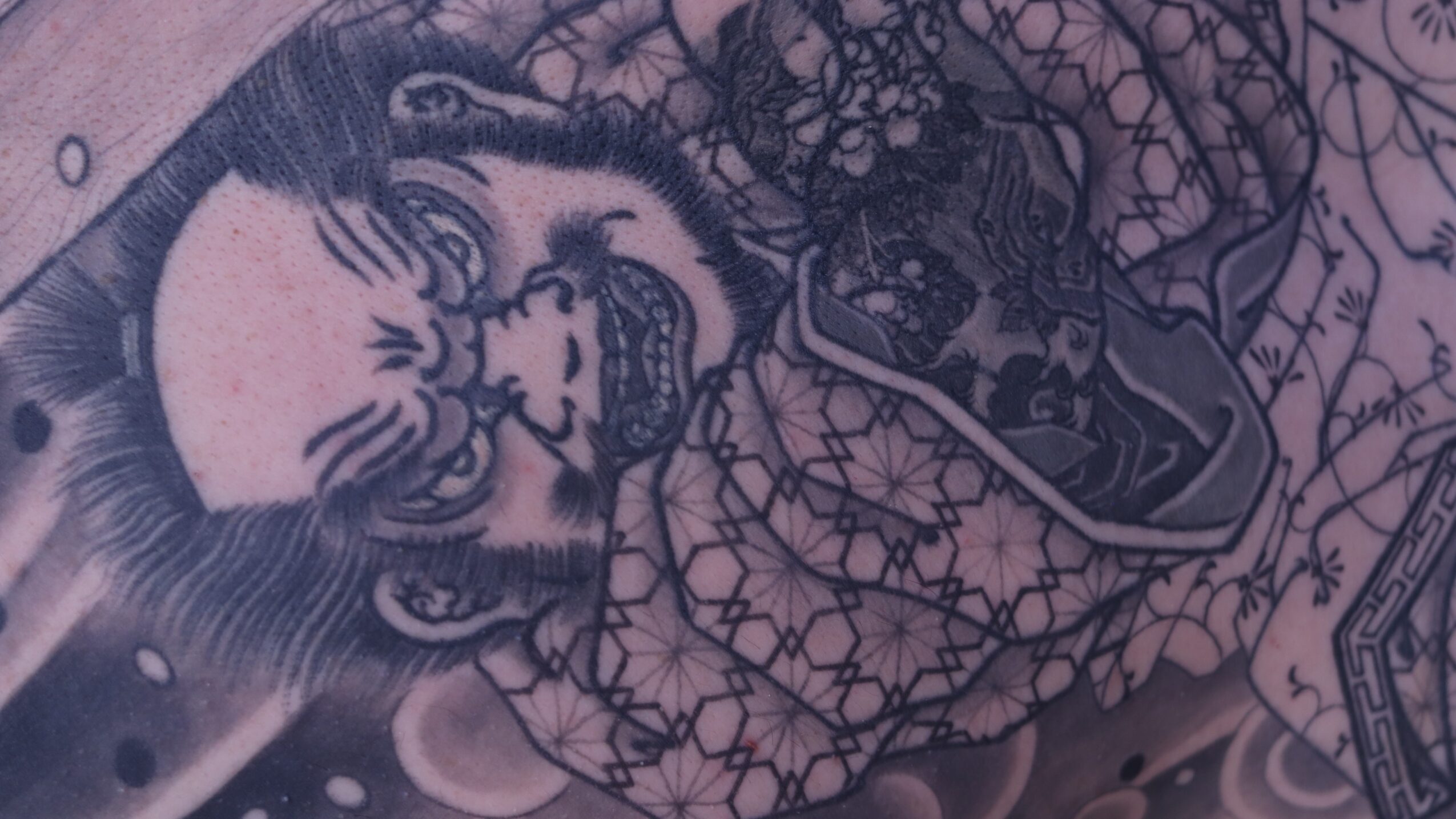 Close-up of a detailed tattoo featuring a person's face with a beard and flowing hair, surrounded by intricate patterns.