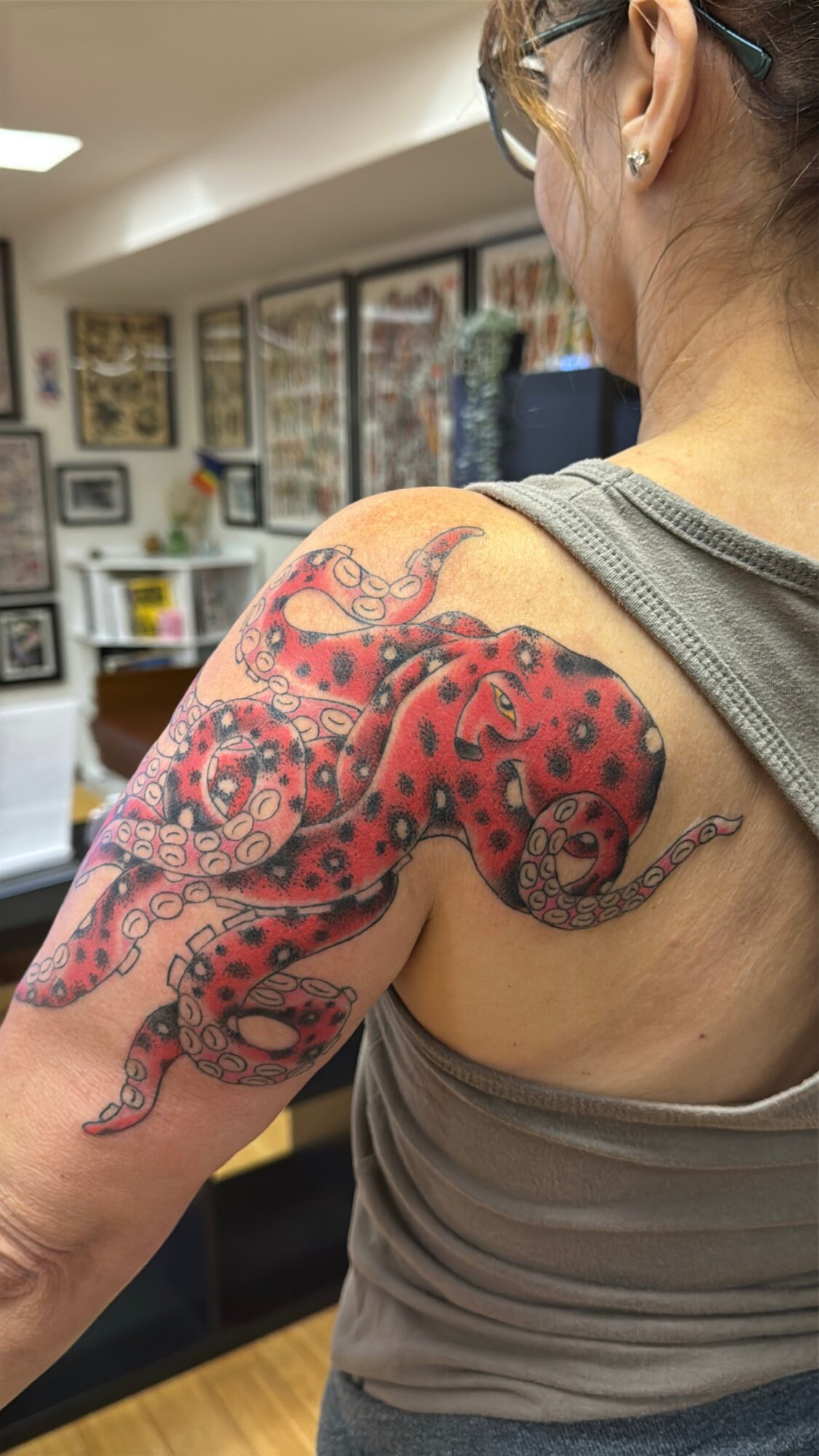 Woman with a colorful snake tattoo on her shoulder and upper arm, in an indoor setting with artwork on walls.